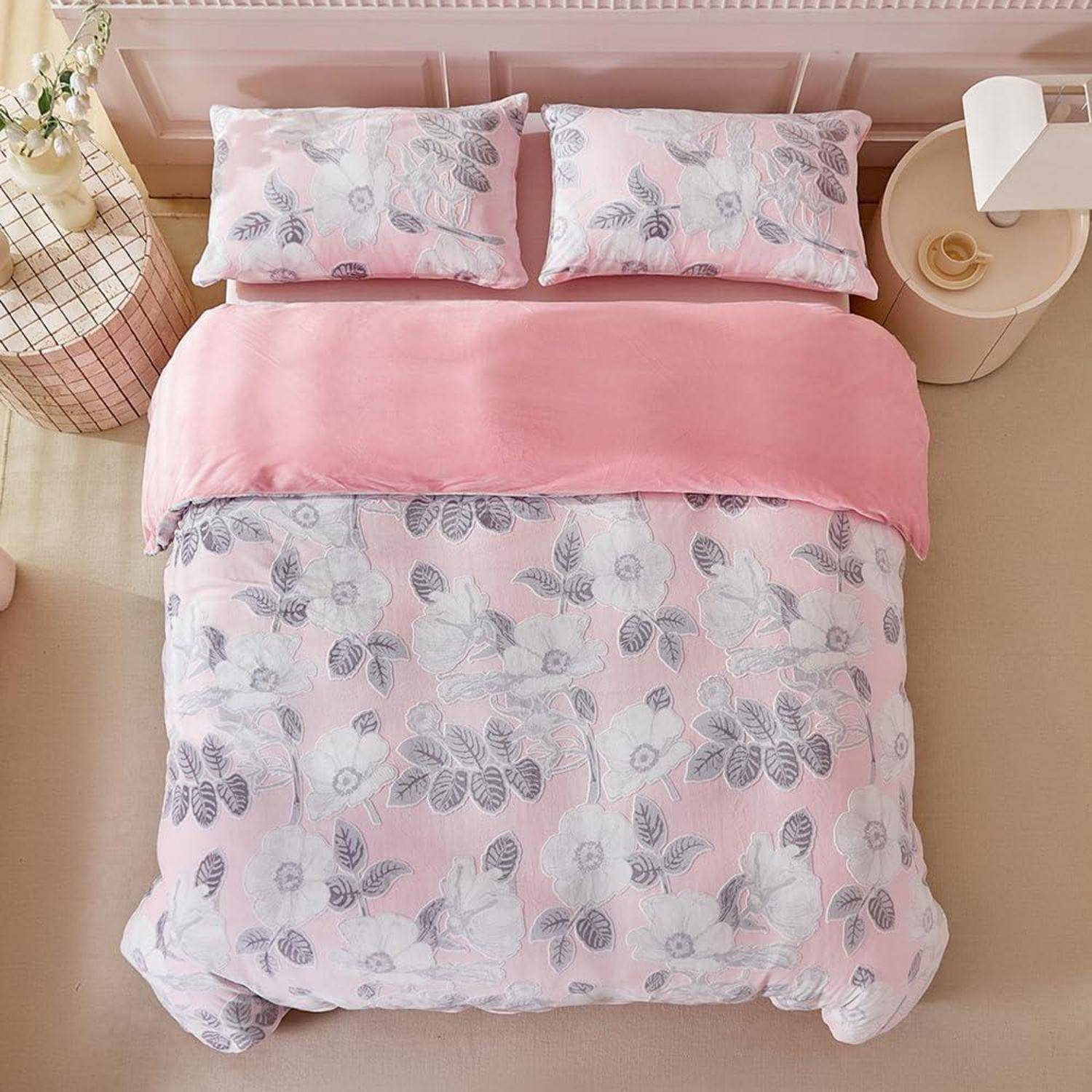 Rosafarbenes Blumenbettwäsche-Set auf einem ordentlich gemachten Bett, mit zwei passenden Kissen, einer einfarbig rosa Bettdecke und Nachttischen auf beiden Seiten.