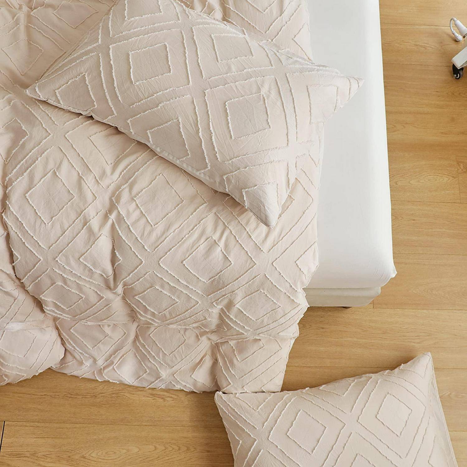 Beige geometrische Steppdecke und passendes Kissen auf einem Bett mit weißem Rahmen und Holzboden.