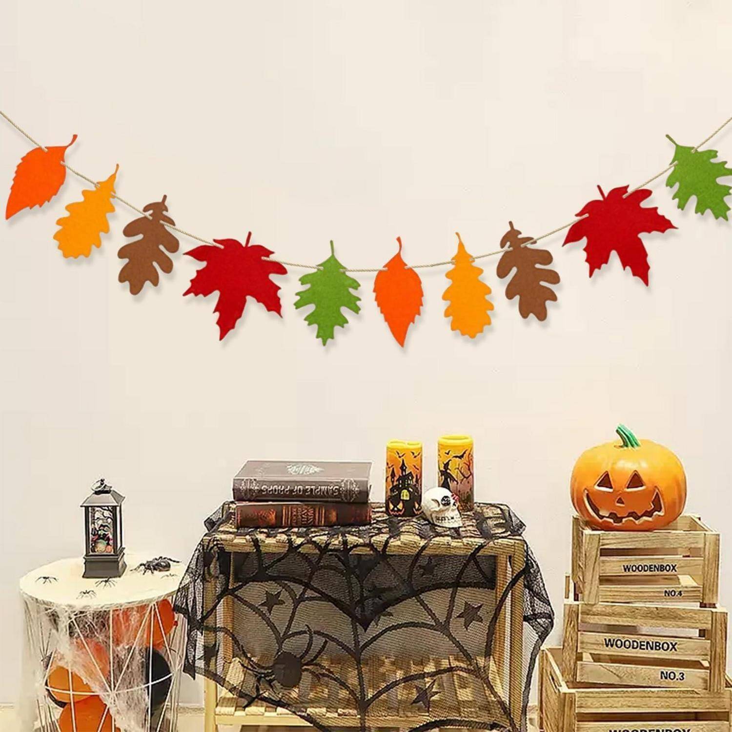 Halloween-Party-Dekoration mit Blattgirlande, mit Spinnweben behangtem Tisch, Kerzen, Totenschädel, Kürbisgesicht und Holzkisten an einer schlichten Wand.
