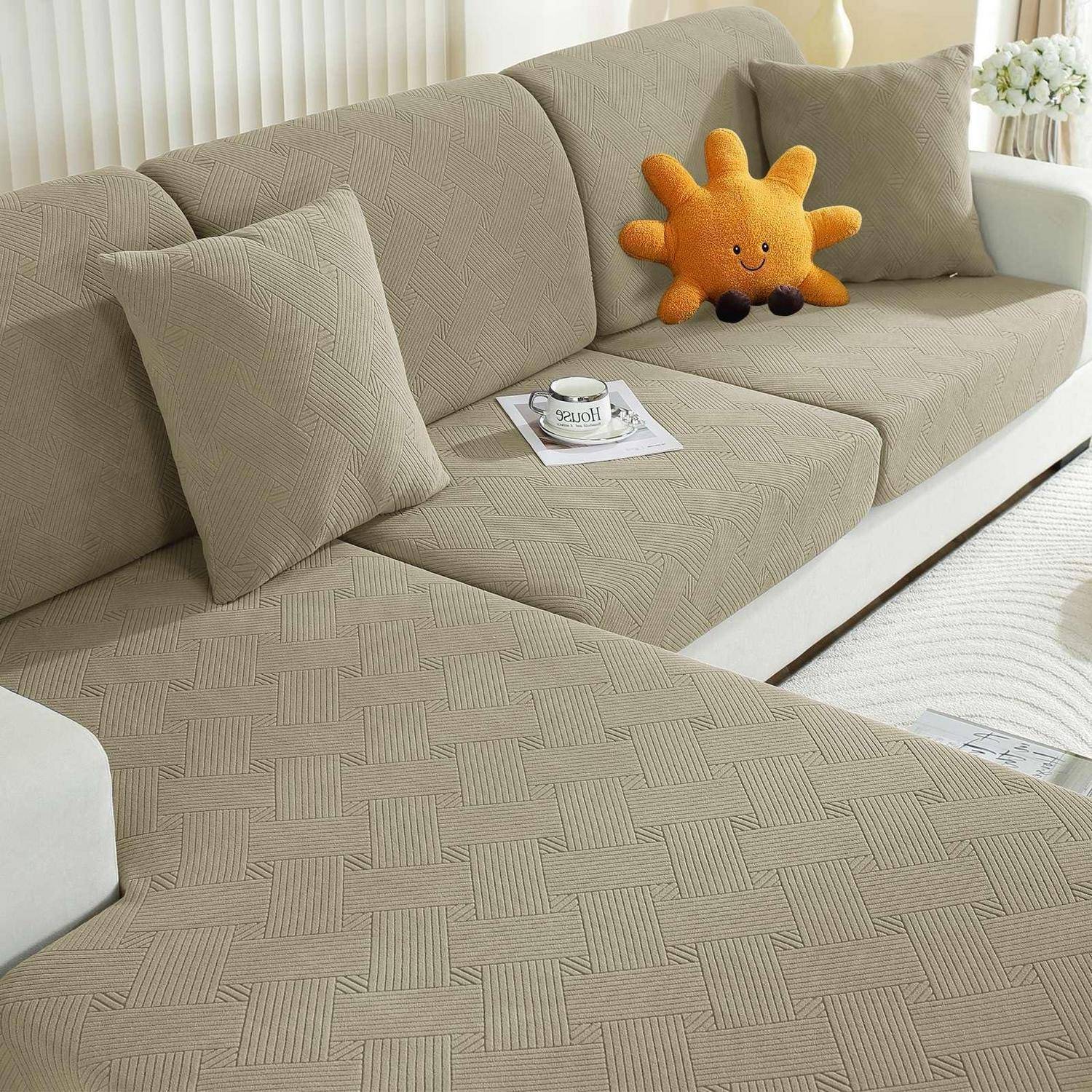 Beigefarbenes Ecksofa mit strukturiertem Bezug, zwei Kissen, eine Kaffeetasse auf einem Magazin und ein orangefarbenes, sonnenförmiges Plüschkissen.