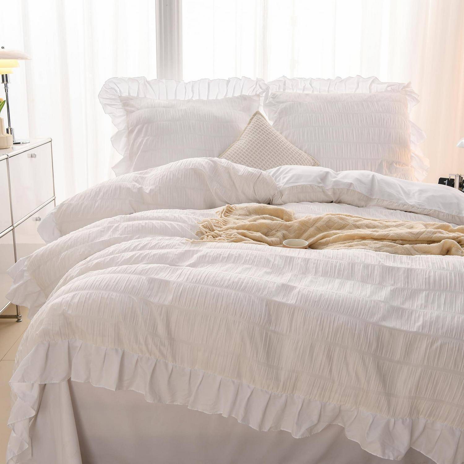 Ein ordentlich gemachtes weißes Bett mit gerüschtem Bettzeug und großen Kissen, sanft von Tageslicht in einem minimalistischen Schlafzimmer beleuchtet.