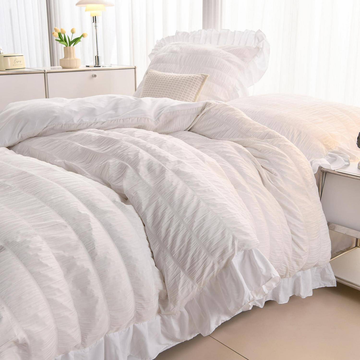Ordentlich gemachtes Bett mit weißer Rüschenbettwäsche in einem hellen, minimalistischen Schlafzimmer neben einem Nachttisch, einer Lampe und Vorhängen.