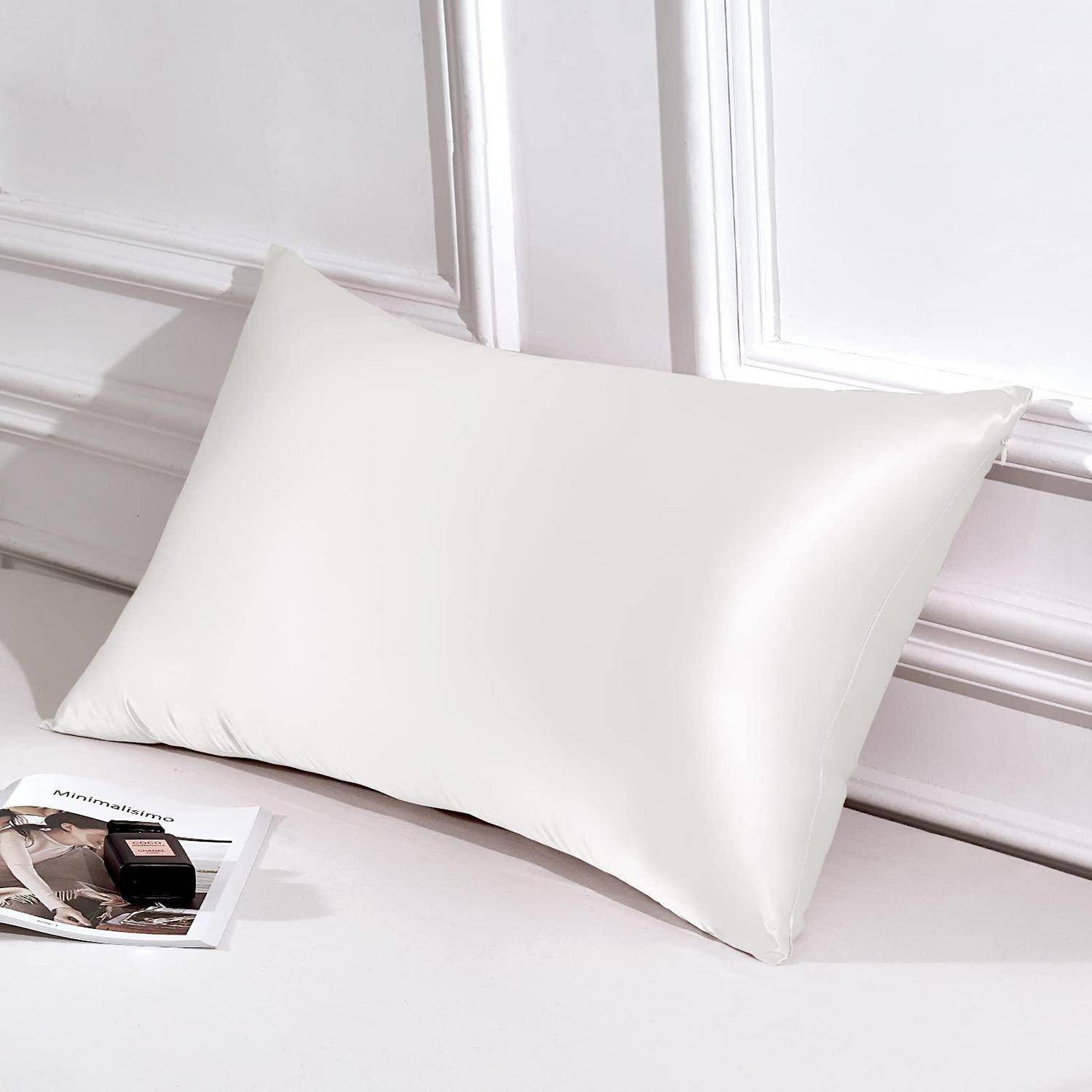 Weißes Satinkissen auf einem Bett neben einer offenen Zeitschrift in einem hellen minimalistischen Schlafzimmer neben einem Fenster.