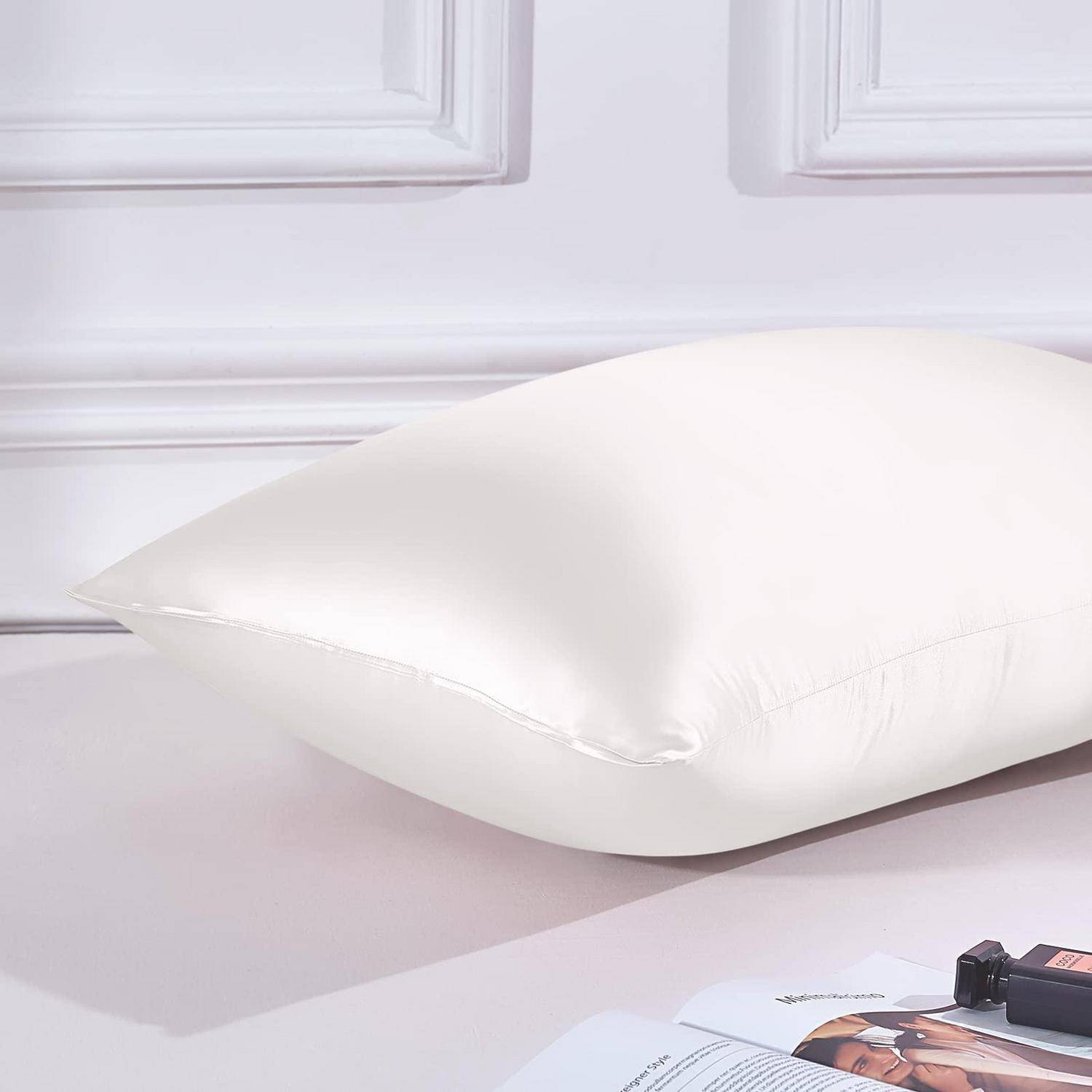 Weißes Kissen auf einem Bett neben bedruckten Papieren und einer kleinen Kamera, was auf eine Produkt- oder Lifestyle-Szene hindeutet.