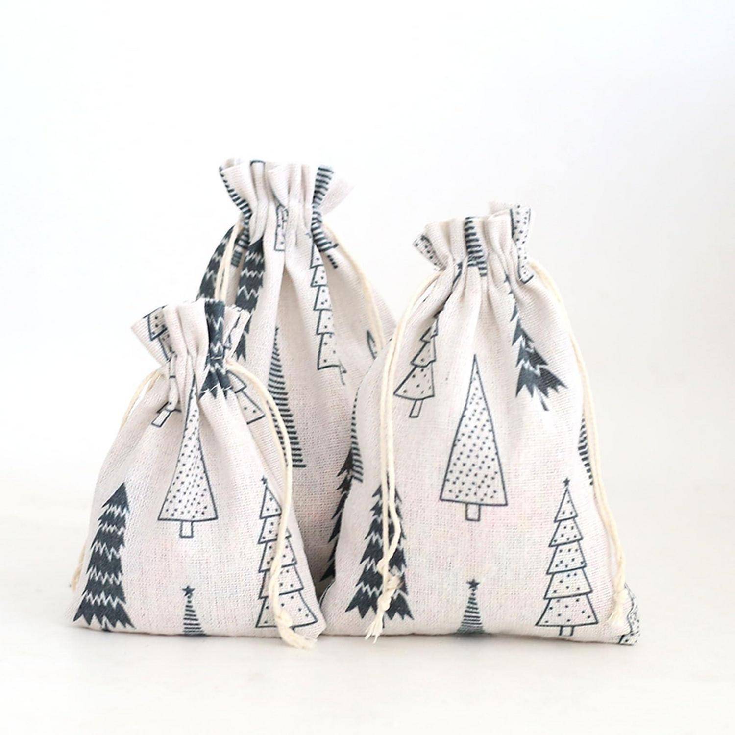 Drei gemusterte Stoffgeschenktaschen mit Kordelzug und Weihnachtsbaumdrucken in verschiedenen Größen, angeordnet auf weißem Hintergrund.