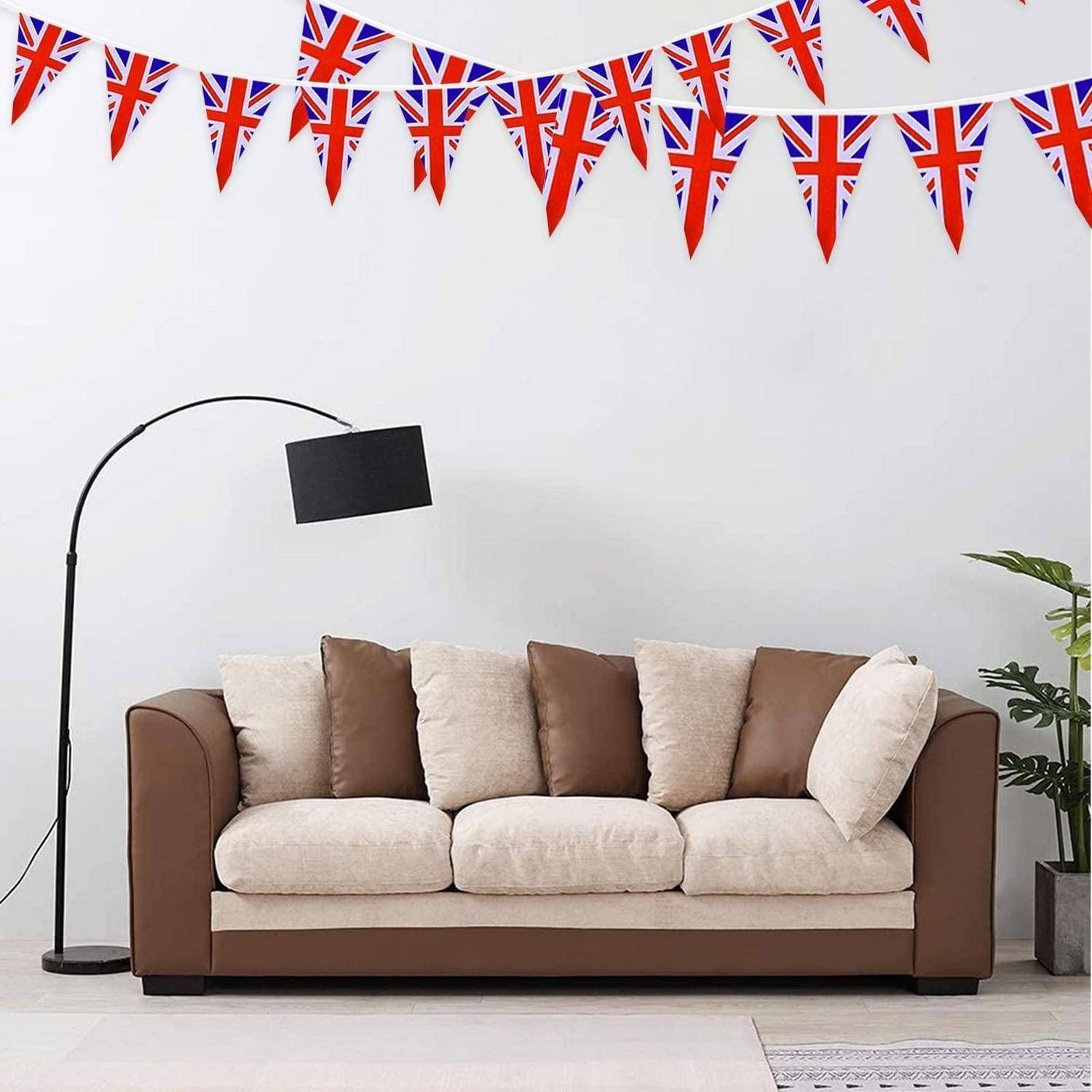 Wohnzimmer im britischen Stil mit Union-Jack-Girlande über einem beige-braunen Sofa und einer Stehlampe; eine Topfpflanze befindet sich auf der rechten Seite.