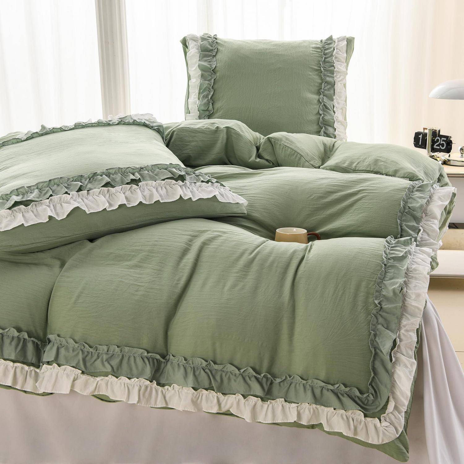 Ein sorgfältig gemachtes Bett mit salbeigrüner gerüschter Steppdecke, Kissen und weißer Borte in einem hellen Schlafzimmer.
