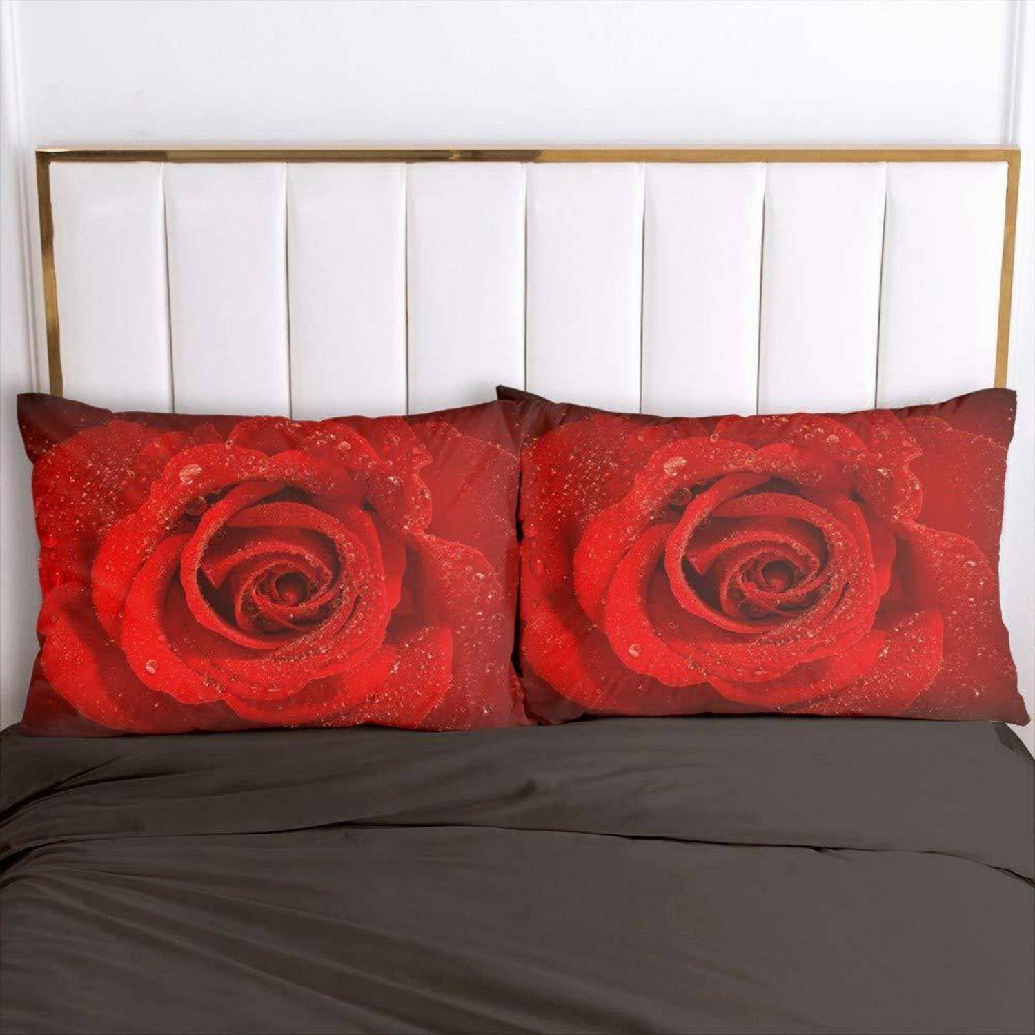 Zwei Kissen auf einem Bett zeigen nahaufnahmen von roten Rosendesigns vor einem weißen Kopfende und dunkler Bettwäsche.