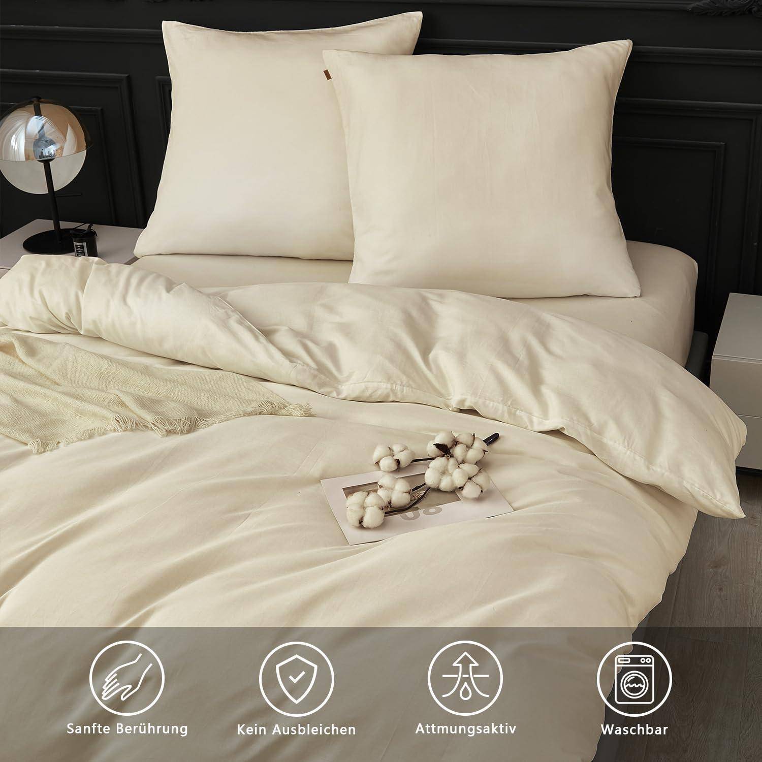 Creme-Bettwäscheset mit zwei Kissen auf einem Bett; Symbole zeigen Weichheit, Farbecht, Atmungsaktivität und Waschbarkeit an.