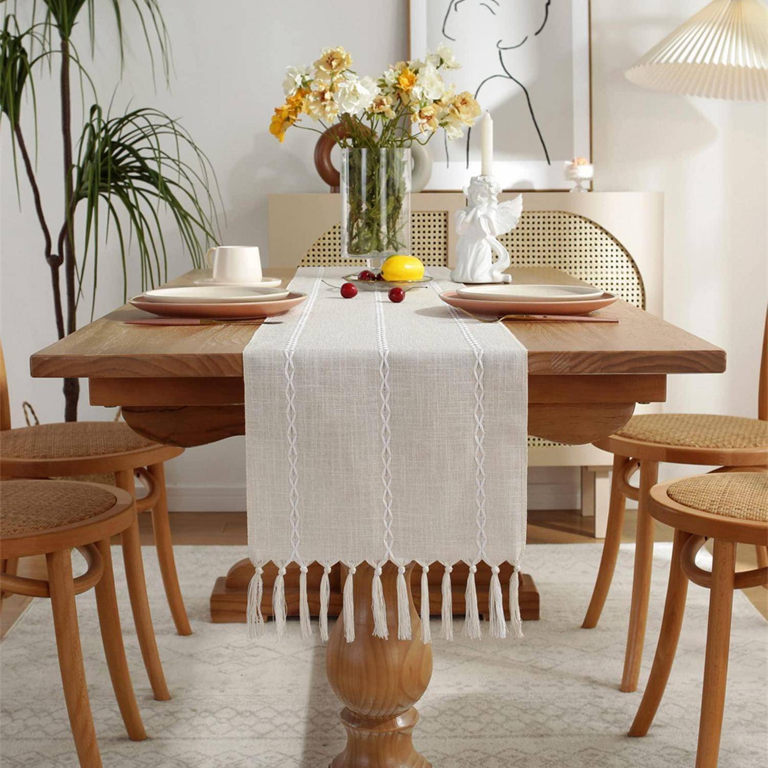Ein stilvolles Esstisch mit weißem Tischläufer, für zwei Personen eingedeckt mit Tellern und Tassen, eine Vase mit Blumen, Zitronen und kleine Dekorationselemente in einem hellen Raum.