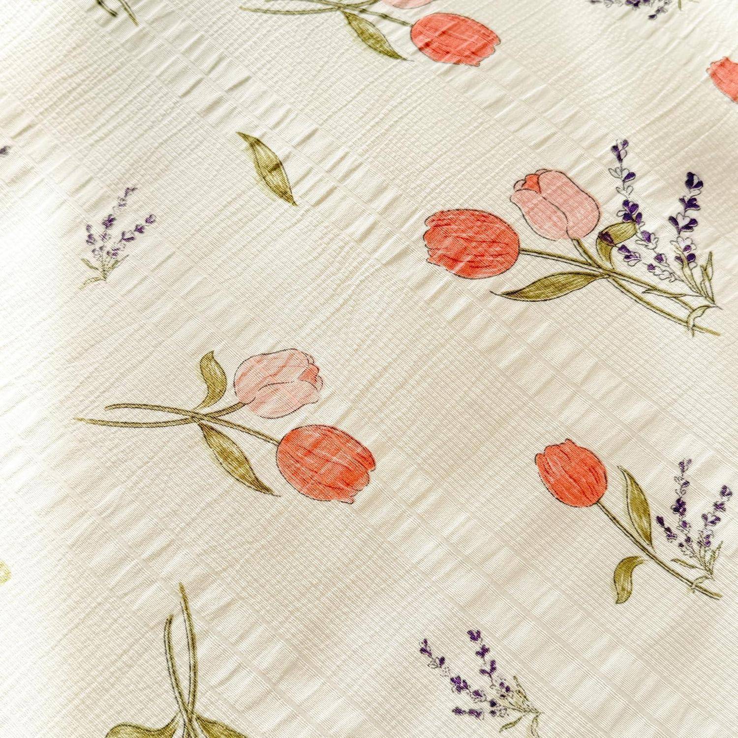 Nahaufnahme eines cremefarbenen gesteppten Stoffs mit bestickten roten und rosa Tulpen und kleinen violetten Blüten, die über das gesamte Muster verstreut sind.