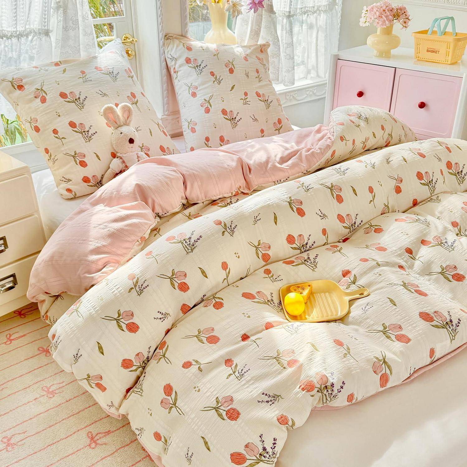 Rosafarbenes Blumen-Bettwäsche-Set auf einem ordentlich gemachten Bett in einem hellen, pastellfarbenen Schlafzimmer, mit passenden Kissen, Bettdecke und Laken.