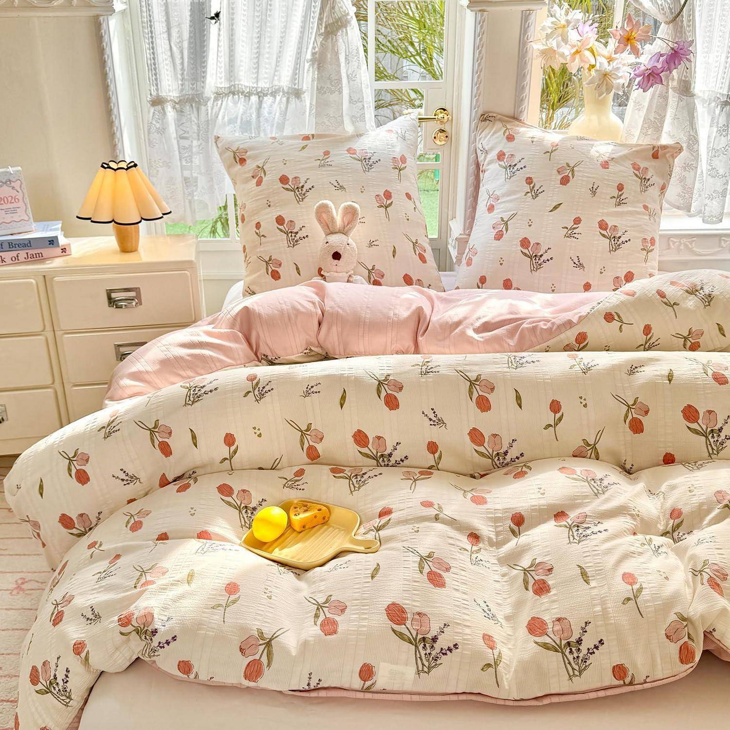 Ein Pastellblumenbett mit rosa Bettwäsche und einem Kuschelhase-Kissen in einem hellen, sonnendurchfluteten Schlafzimmer.