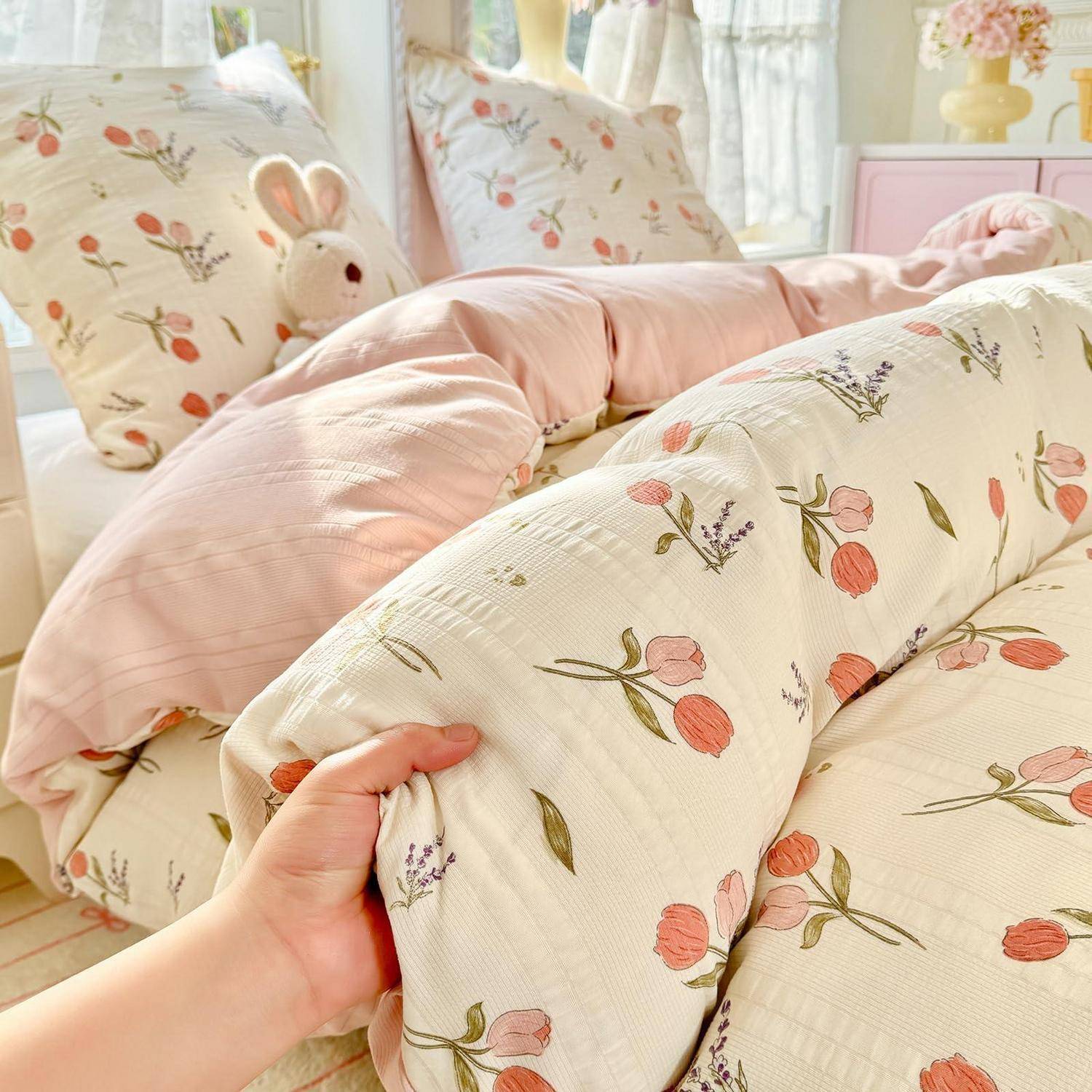 Hand hält einen floralen Baby-Lounger mit rosa Kissen und Häschenkissen in einem hell eingerichteten Kinderzimmer.
