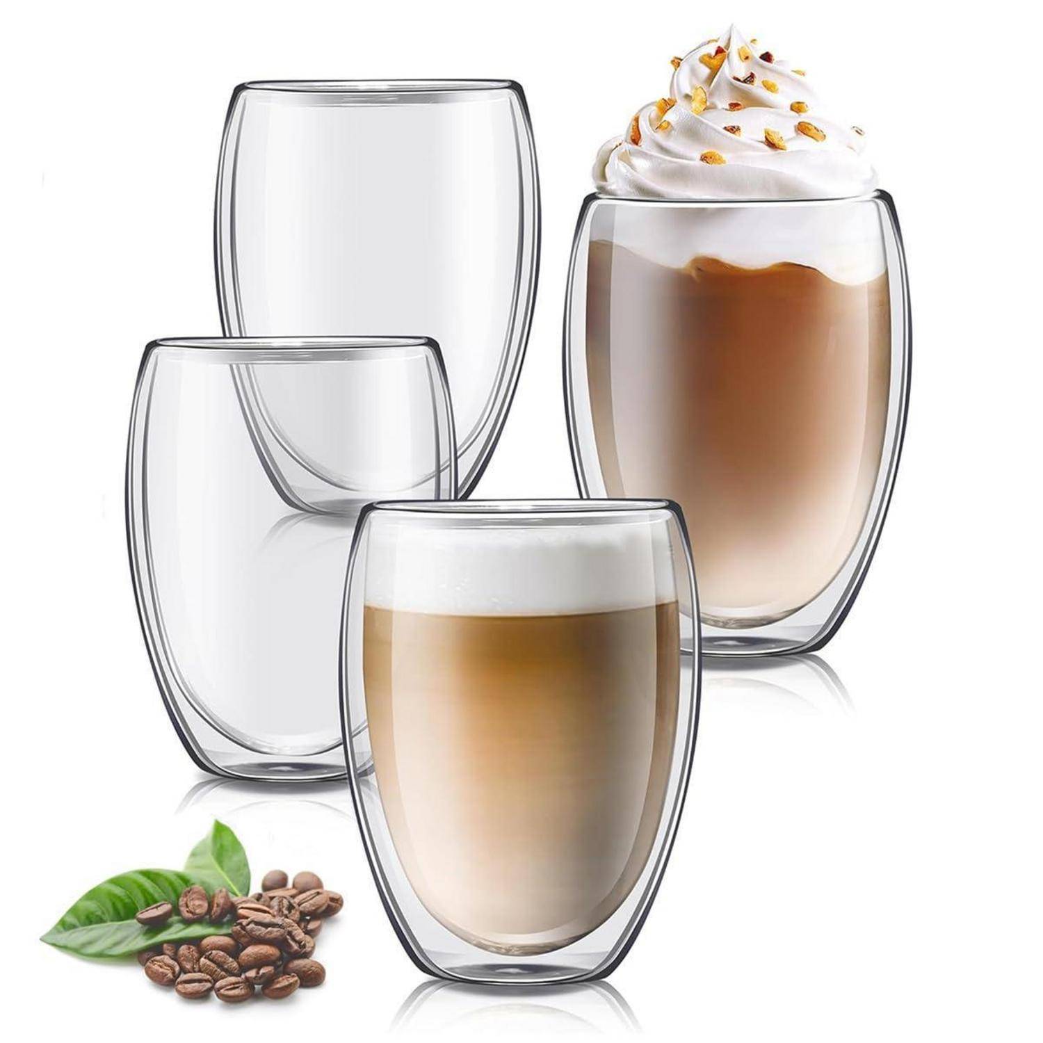 Satz aus doppelwandigen Glaskaffeetassen, einschließlich einer mit Latte-Schaum und Schlagsahne, plus Kaffeebohnen und Blätter.
