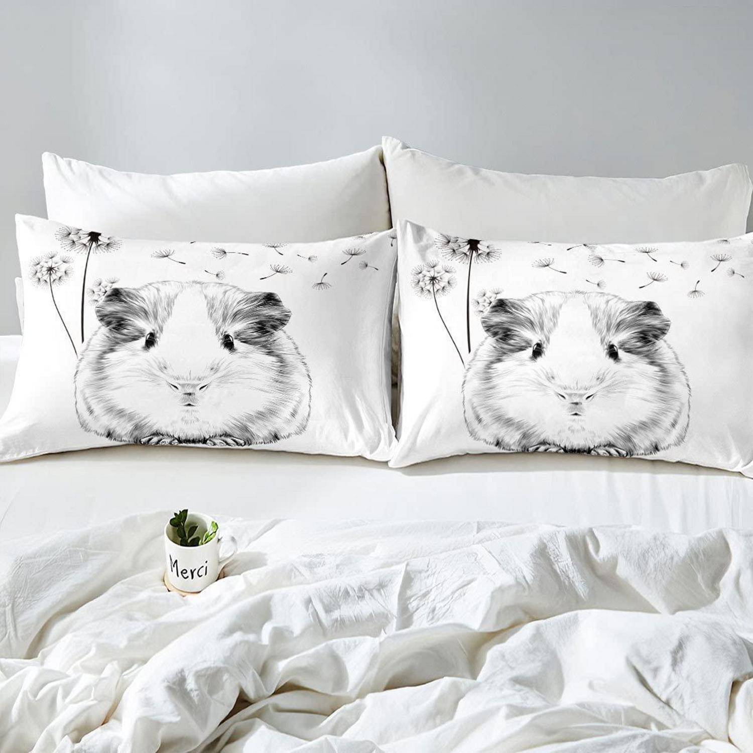 Zwei weiße Bettkissen mit Meerschweinchen-Motiven auf einem ordentlich gemachten weißen Bett, mit einem kleinen 'Merci'-Blumentopf im Vordergrund.