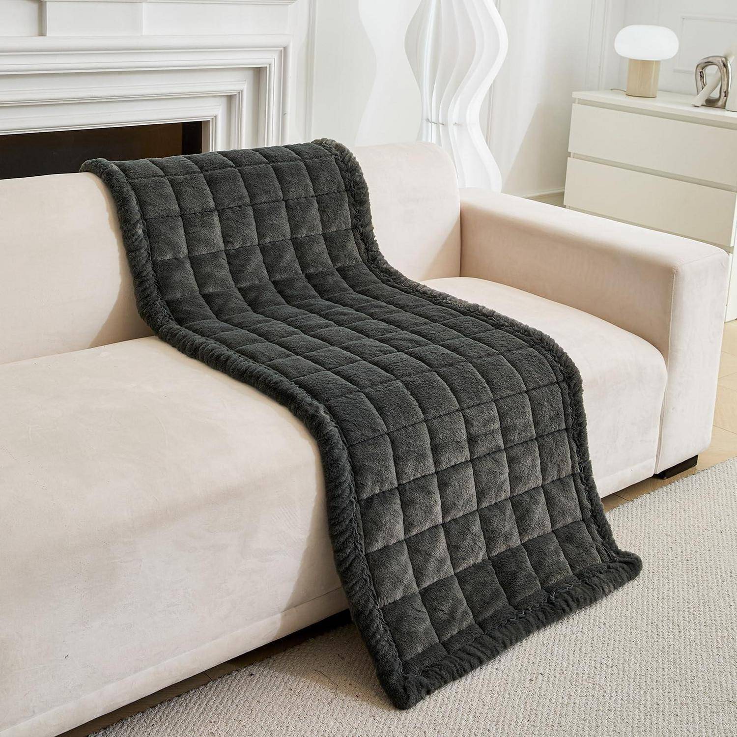 Dunkelgraue gesteppte Wurfdecke, die über ein beiges Sofa in einem hellen, modernen Wohnzimmer drapiert ist.