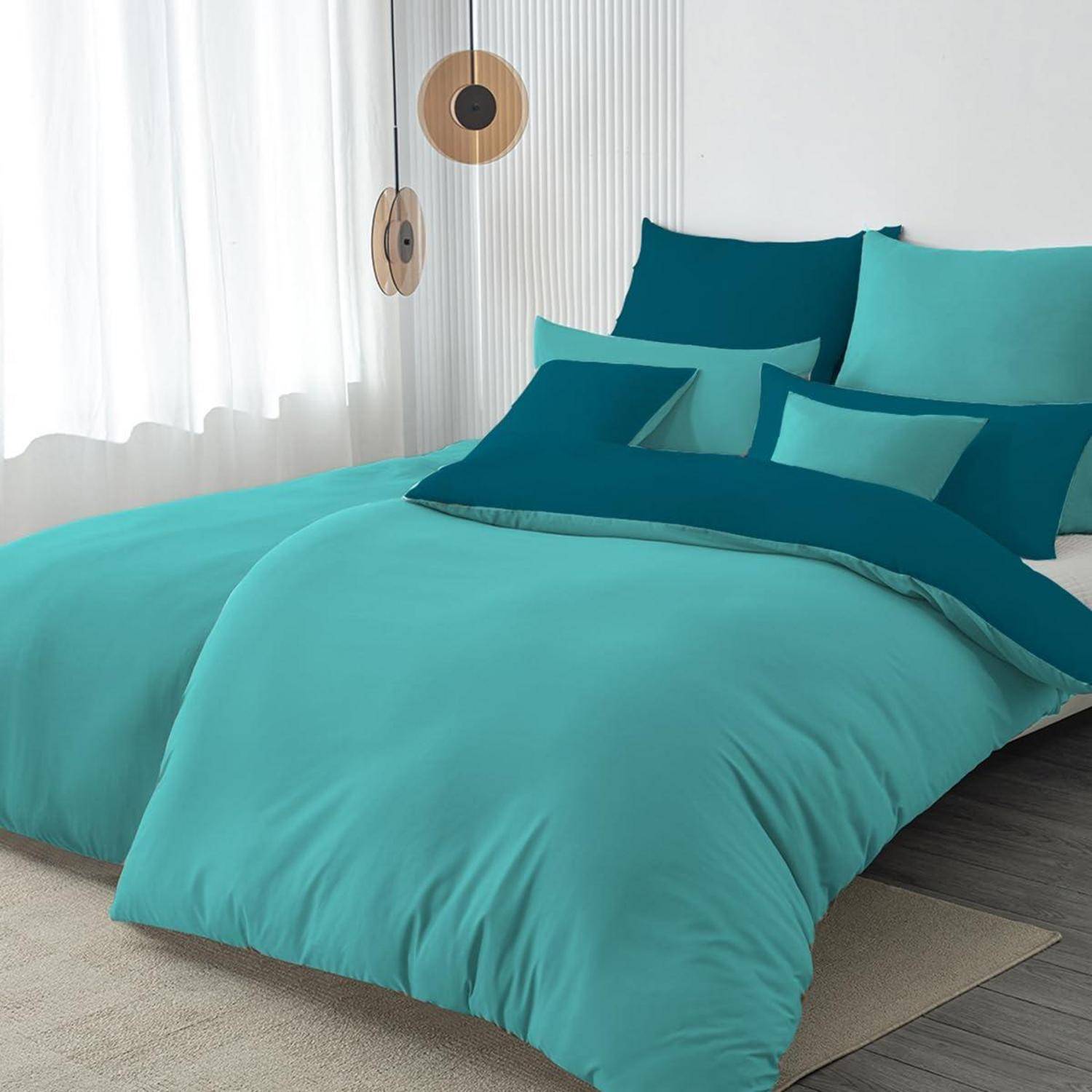 Ein ordentlich gemachtes Bett mit türkisfarbenem und blaugrünem Bettwäsche und passenden Kissen in einem hell eingerichteten modernen Schlafzimmer.