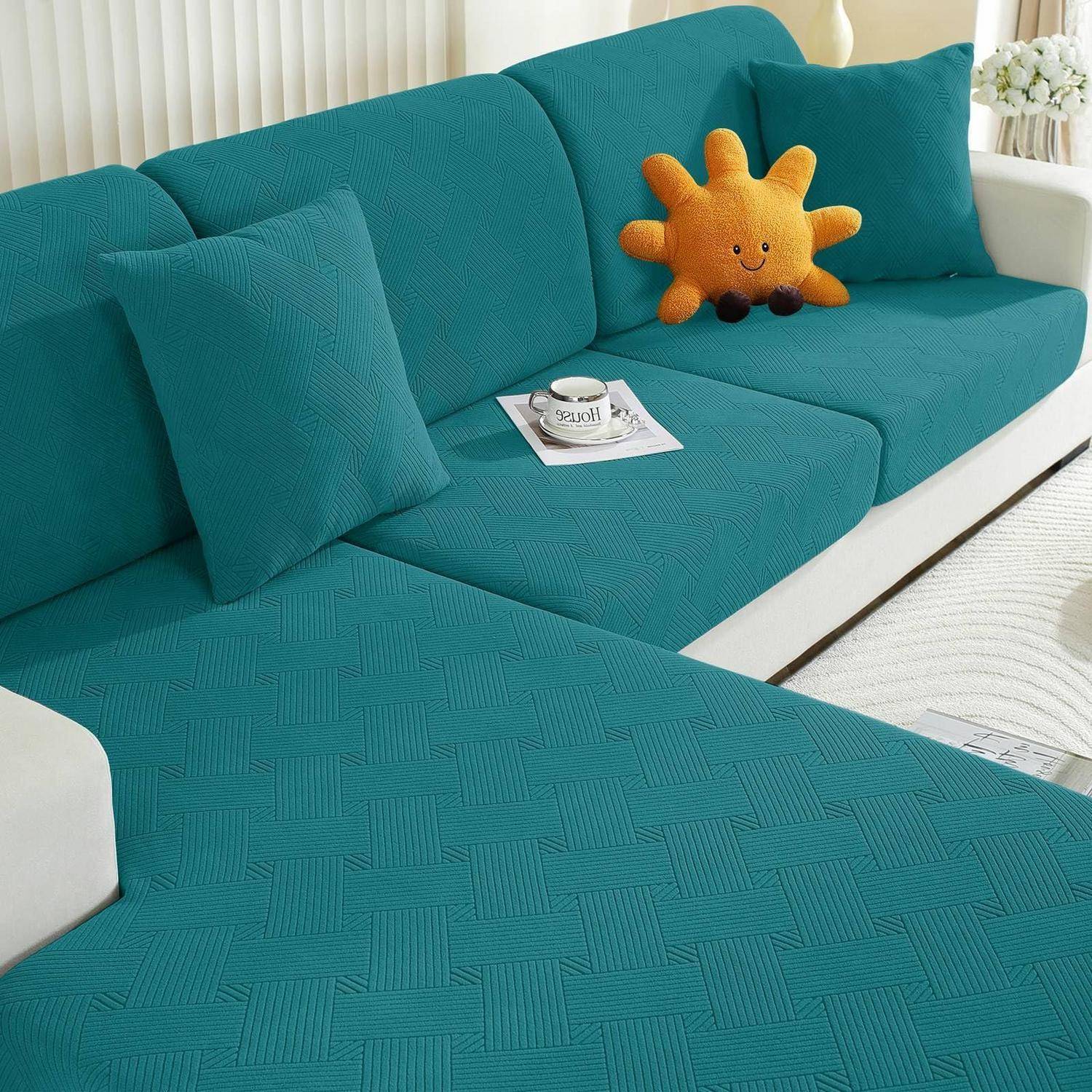 Tealfarbenes Ecksofa mit passenden Kissen und orangefarbenem Sonnenkissen in einem hellen Wohnzimmer, mit einer Tasse auf einem Tablett.