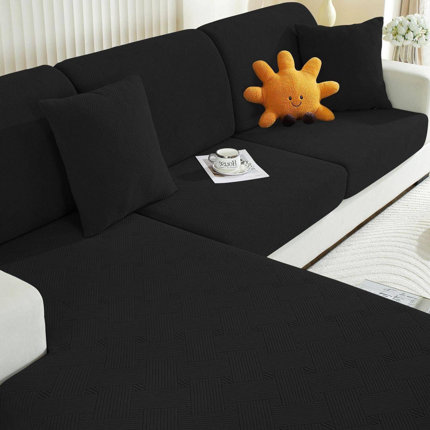 Schwarzes Ecksofa mit schwarzen Kissen, einem orangefarbenen lächelnden Sonnenkissen und einer Tasse auf einem Tablett.