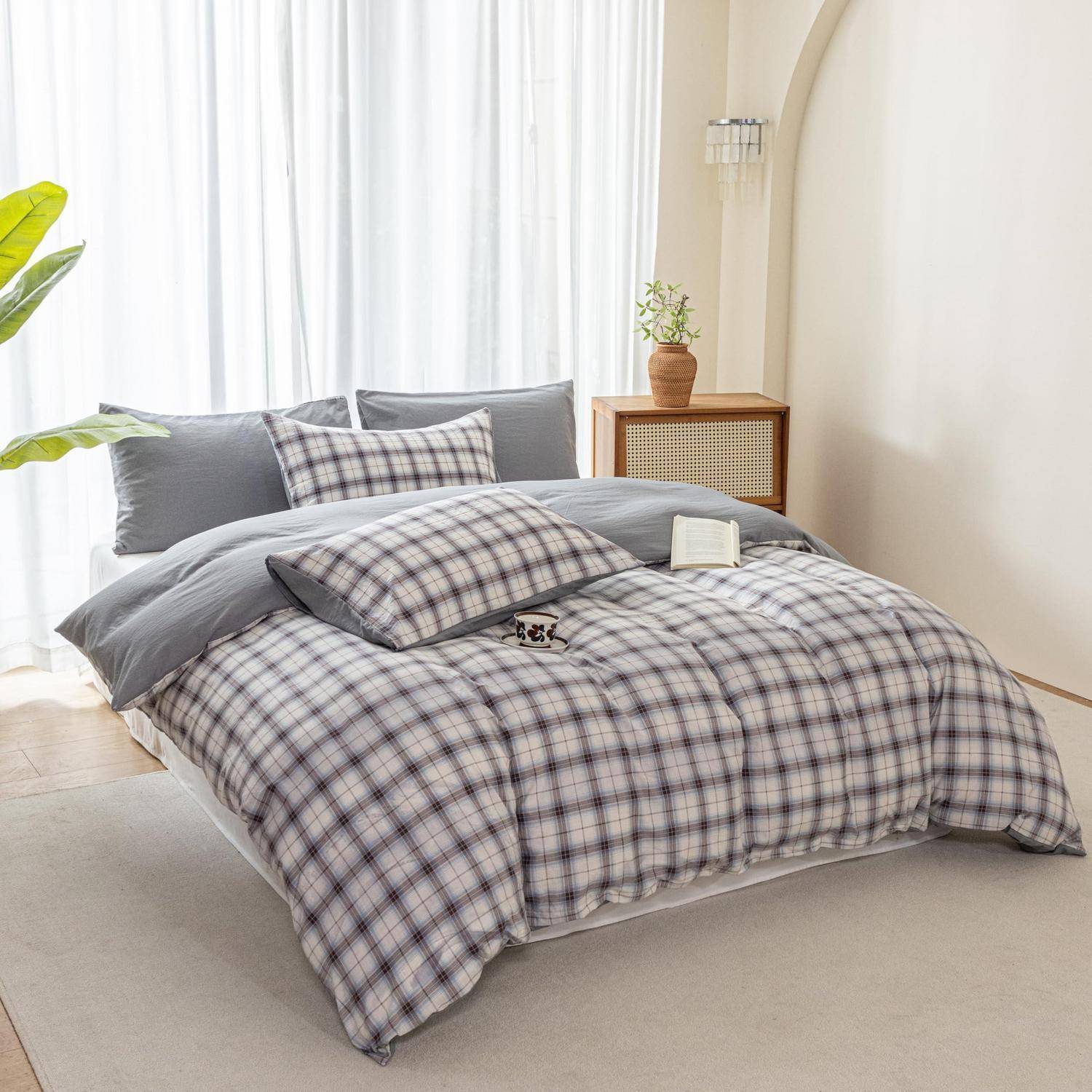 Ordentlich gemachtes Bett mit grauer Karo-Bettwäsche und Kissen neben einem kleinen Nachttisch mit einer Pflanze in einem hellen, minimalistischen Schlafzimmer.