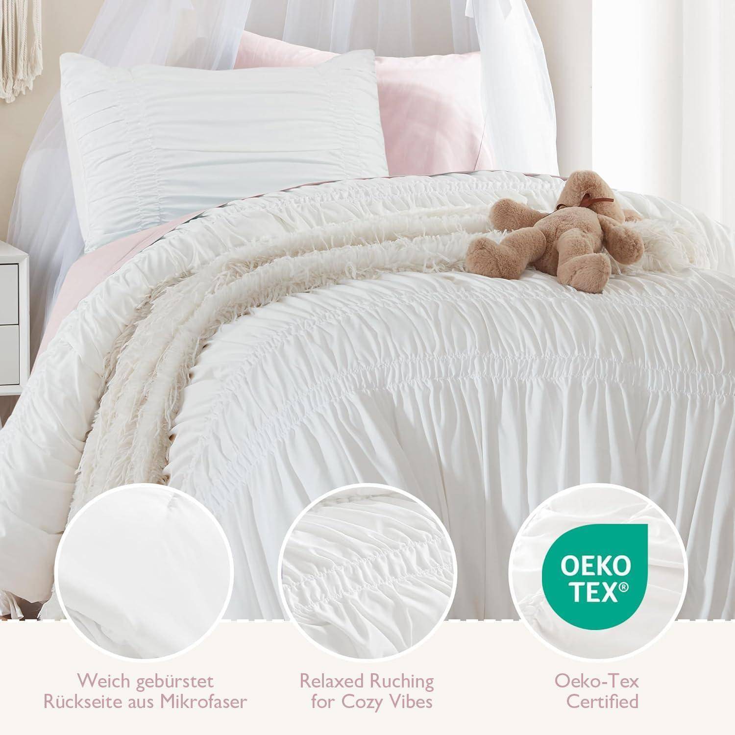 Weiße geraffelte Bettwäsche auf einem gemachten Bett mit einem Teddybär, das Stoffmerkmale zeigt: 'Weich gebürstet', 'Relaxed Ruching for Cozy Vibes' und Oeko-Tex zertifiziert.
