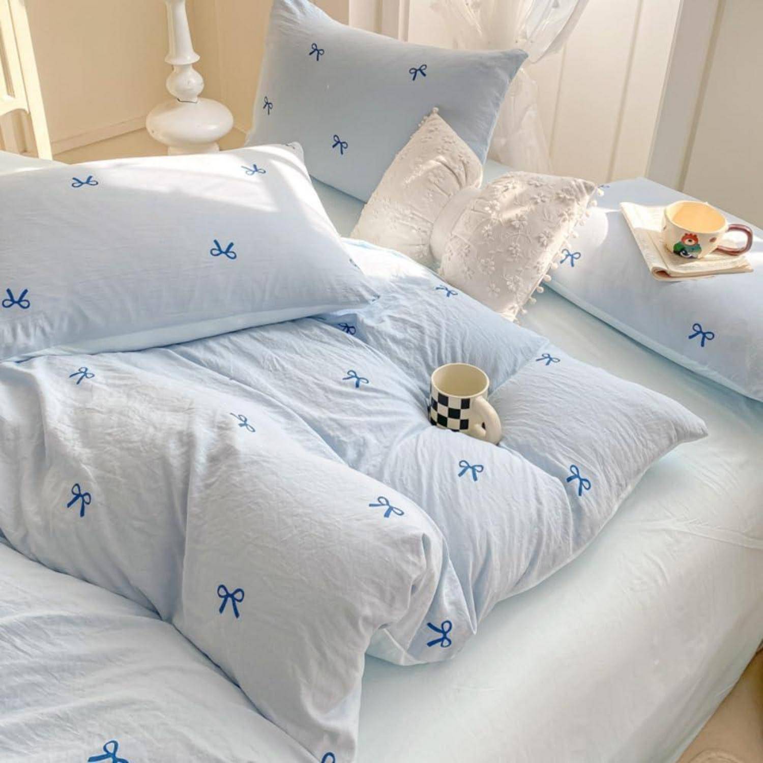 Ein Bett mit hellblauem Schleifendruck-Bettwäsche, Kissen und zwei Tassen auf einem weichen, ordentlich gestylten Bettdecke.