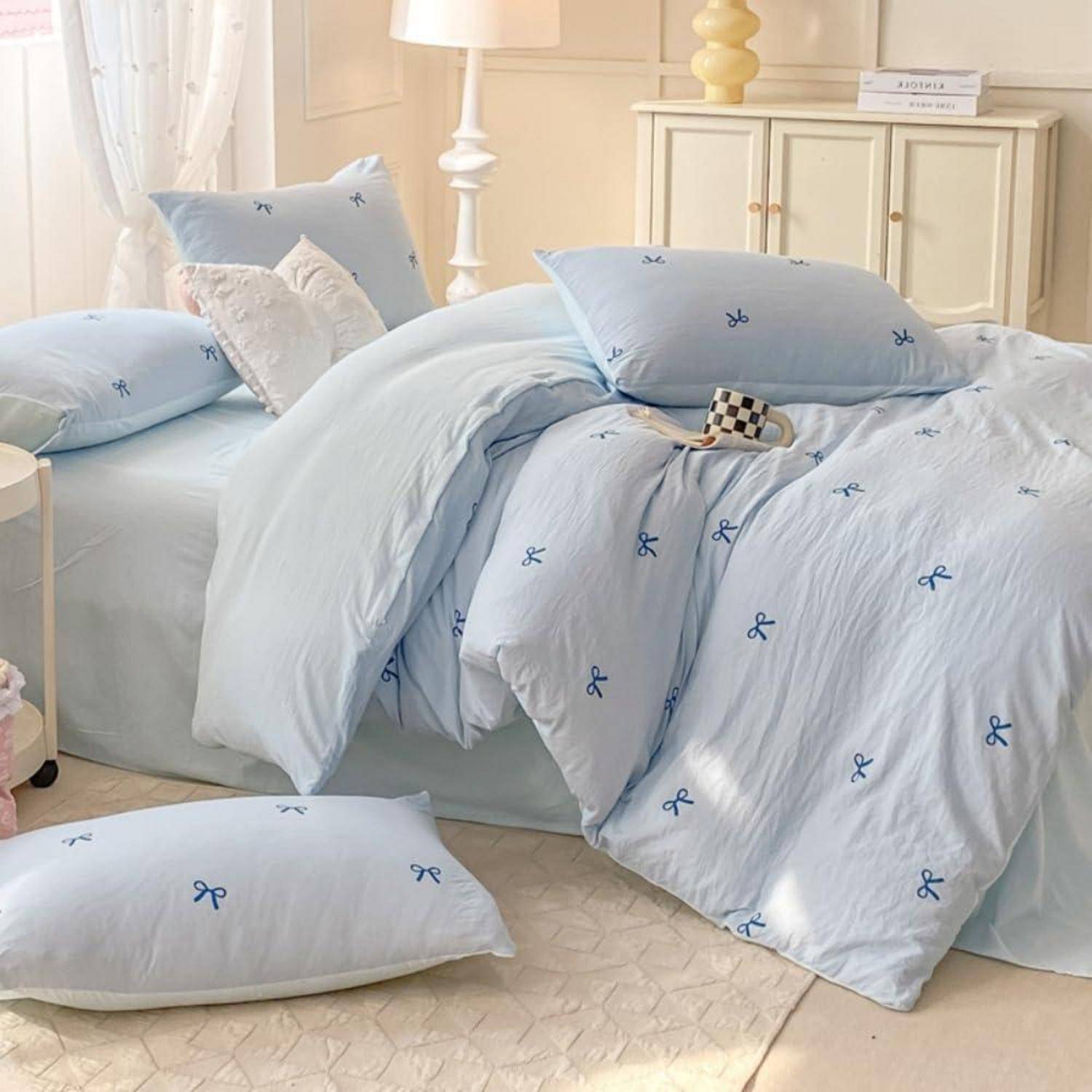 Ein ordentlich gemachtes Bett mit hellblauer Bettwäsche mit Schleifenmuster und passenden Kissen in einem weichen, cremefarbenen Schlafzimmer.
