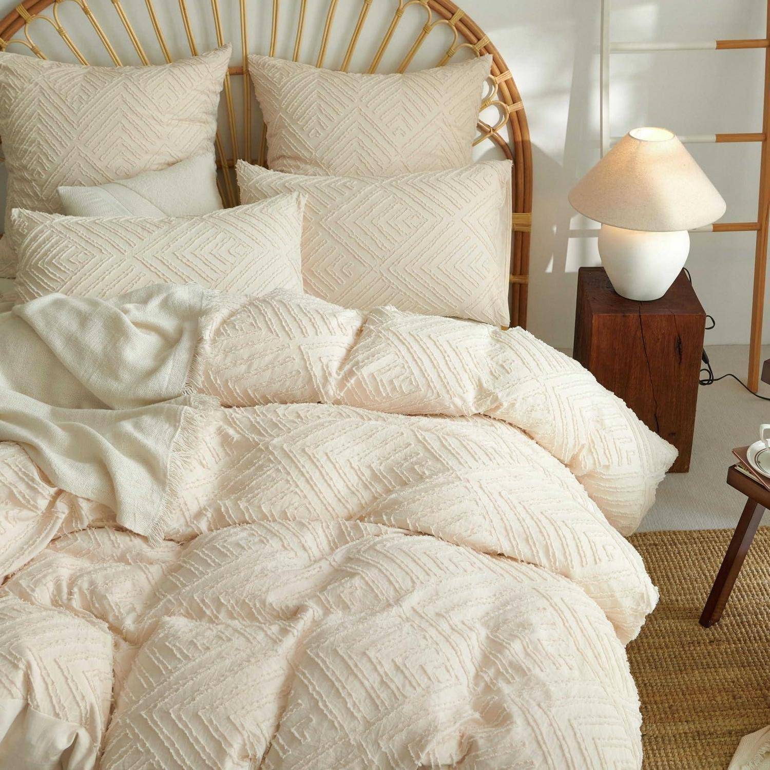 Cremefarbene strukturierte Bettwäsche mit Kissen auf einem gewebten Kopfende eines Bettes neben einer Lampe auf einem Holznachttisch in einem hellen Schlafzimmer.