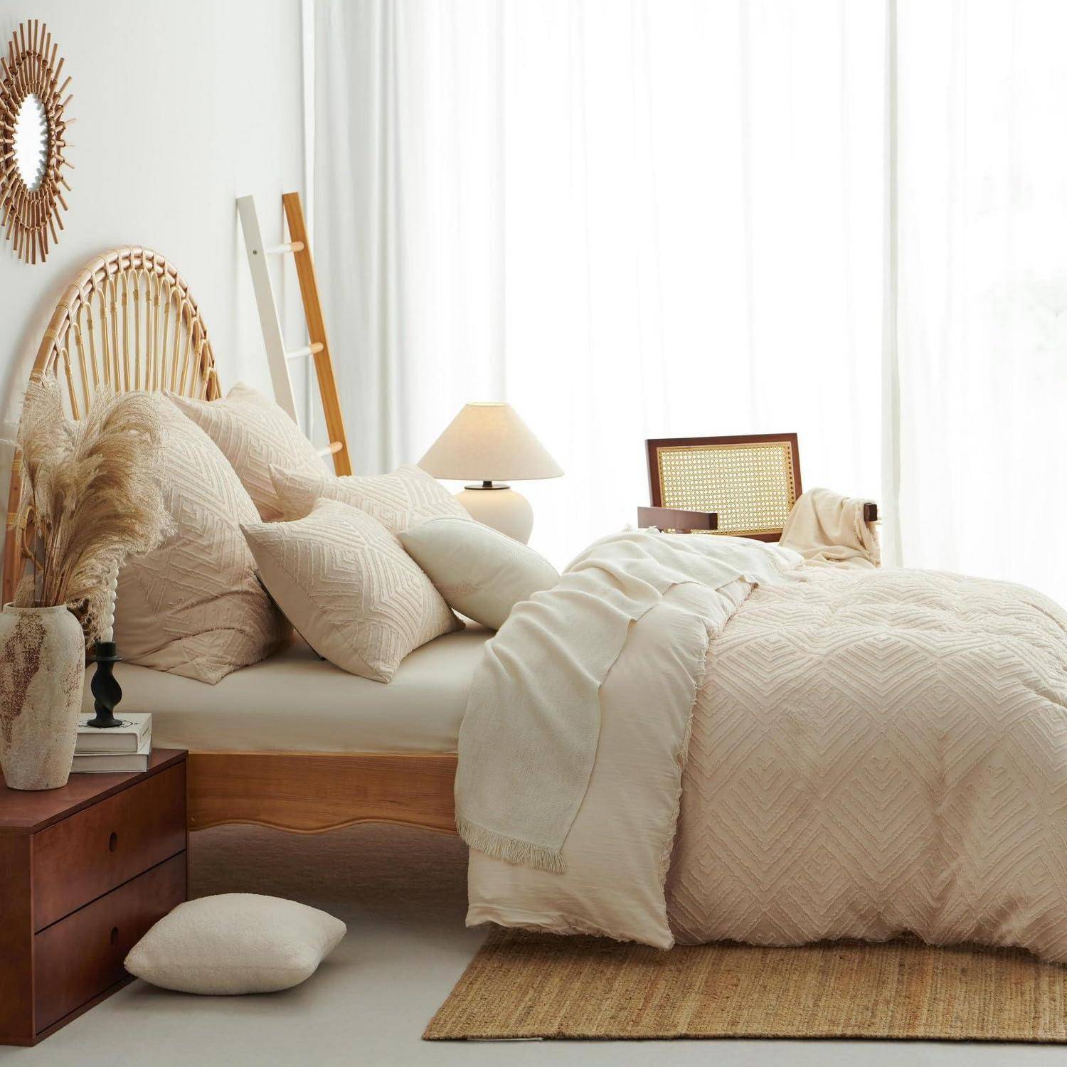 Helles, gemütliches Schlafzimmer mit einem ungemachten cremefarbenen Bett, Rattankopfteil, Kissen, Lampe, Nachttisch und gewebtem Teppich neben durchsichtigen Vorhängen.