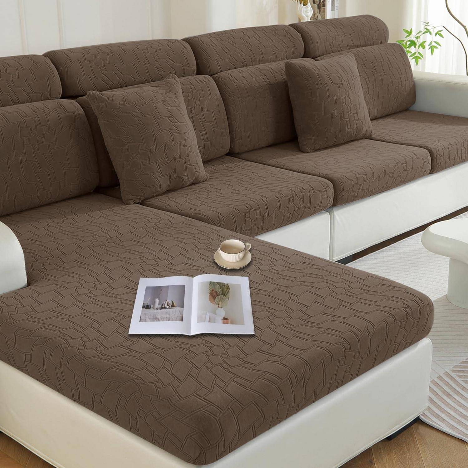 Braunes Ecksofa mit passenden Kissen und Hocker, ein offenes Magazin und eine Tasse darauf in einem hellen Wohnzimmer.