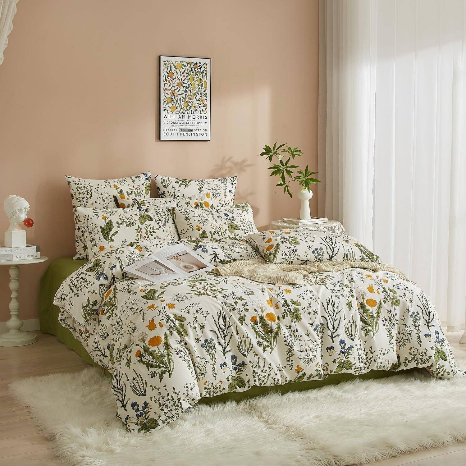 Blumenbettwäsche auf einem niedrigen Bett in einem sanft beleuchteten Pastellschlafzimmer mit gerahmten Wandbildern, Beistelltischen, Vorhängen und einem weißen Teppich.