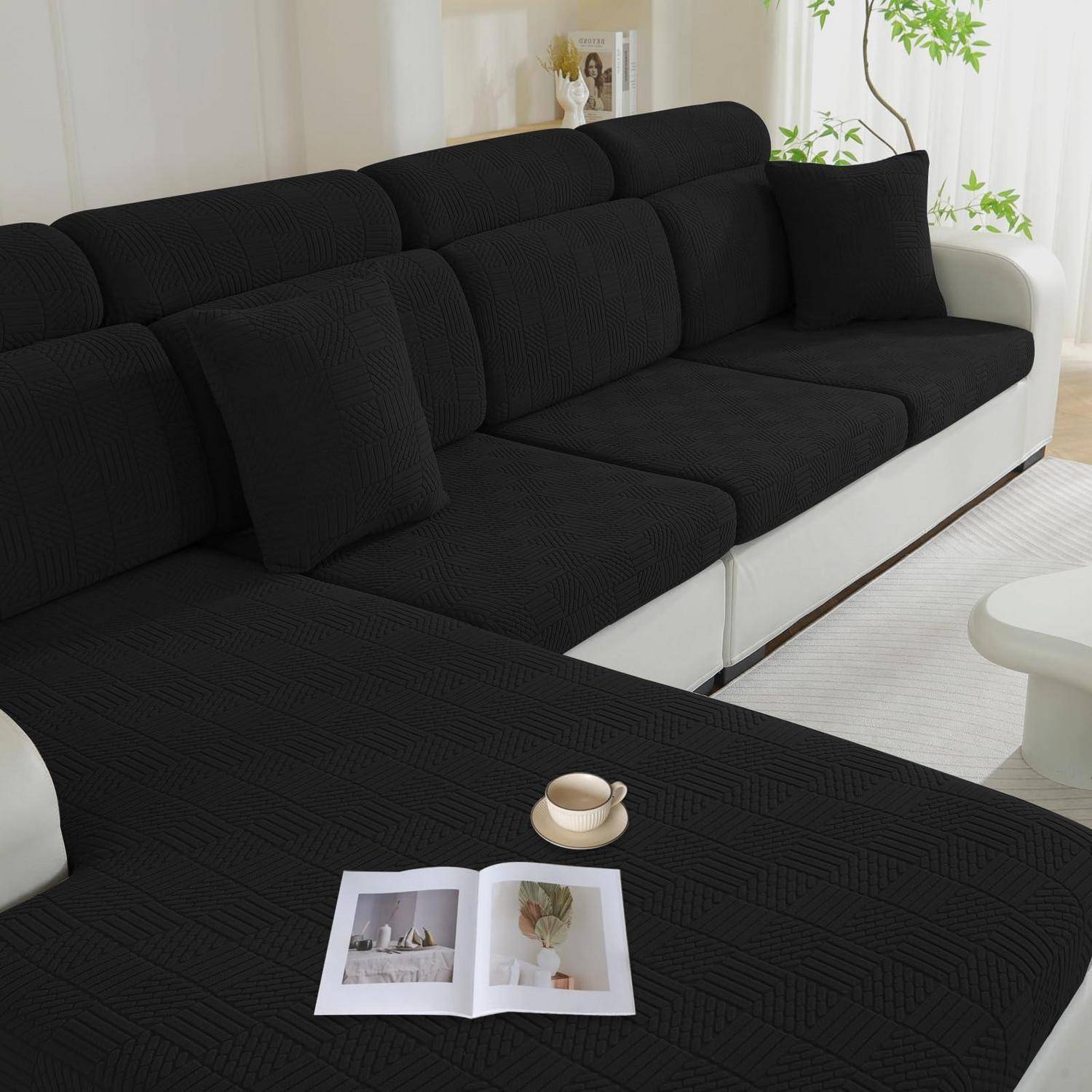 Schwarzes Ecksofa mit weißer Basis in einem hellen Wohnzimmer, mit einer offenen Zeitschrift und einer Teetasse auf dem Hocker.