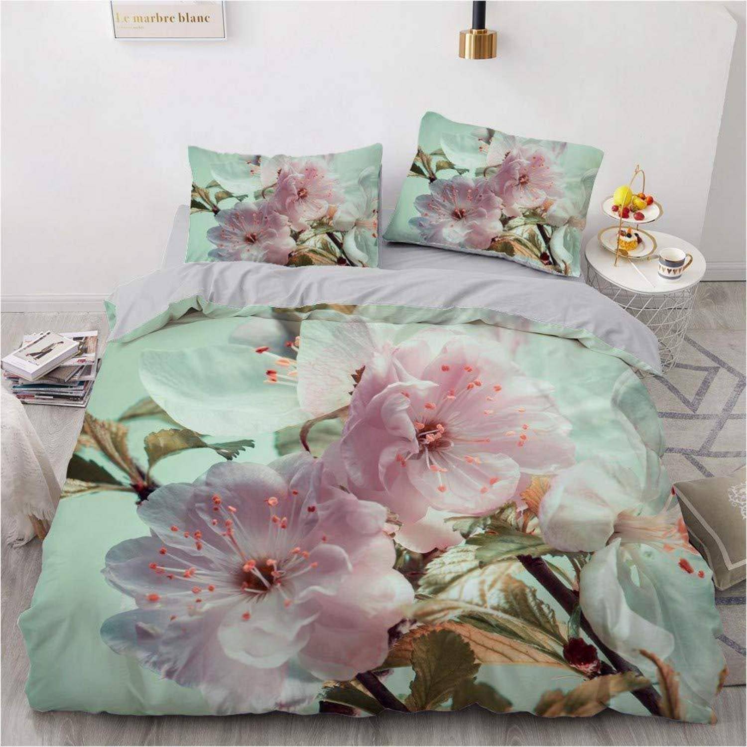 Ein Bett mit mintgrüner Blumenbettwäsche und zwei passenden Kissenbezügen mit großen rosa Blüten in einem hellen, minimalistischen Schlafzimmer.