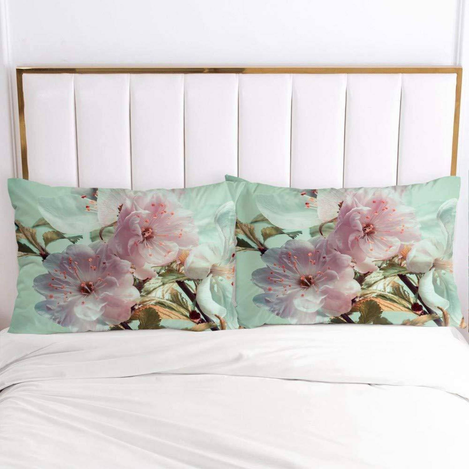 Ein ordentlich gemachtes Bett mit weißem Kopfteil, weißer Bettwäsche und zwei passenden Kissen mit Blumenmuster, die rosa Blüten auf mintgrünem Hintergrund zeigen.
