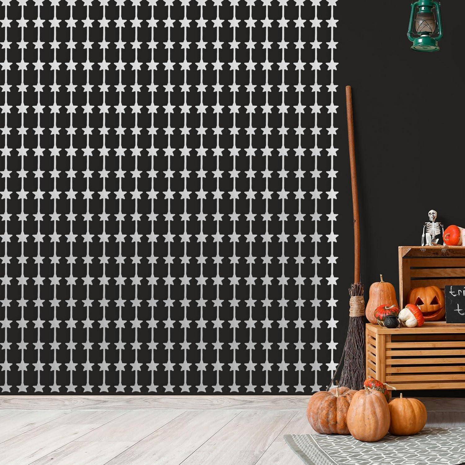 Dekorative Halloween-ähnliche Herbstdekoration mit Kürbissen, Besen, Skelettfigur, Laterne und Holzkisten vor einer schwarzen Wand mit Sternmuster.