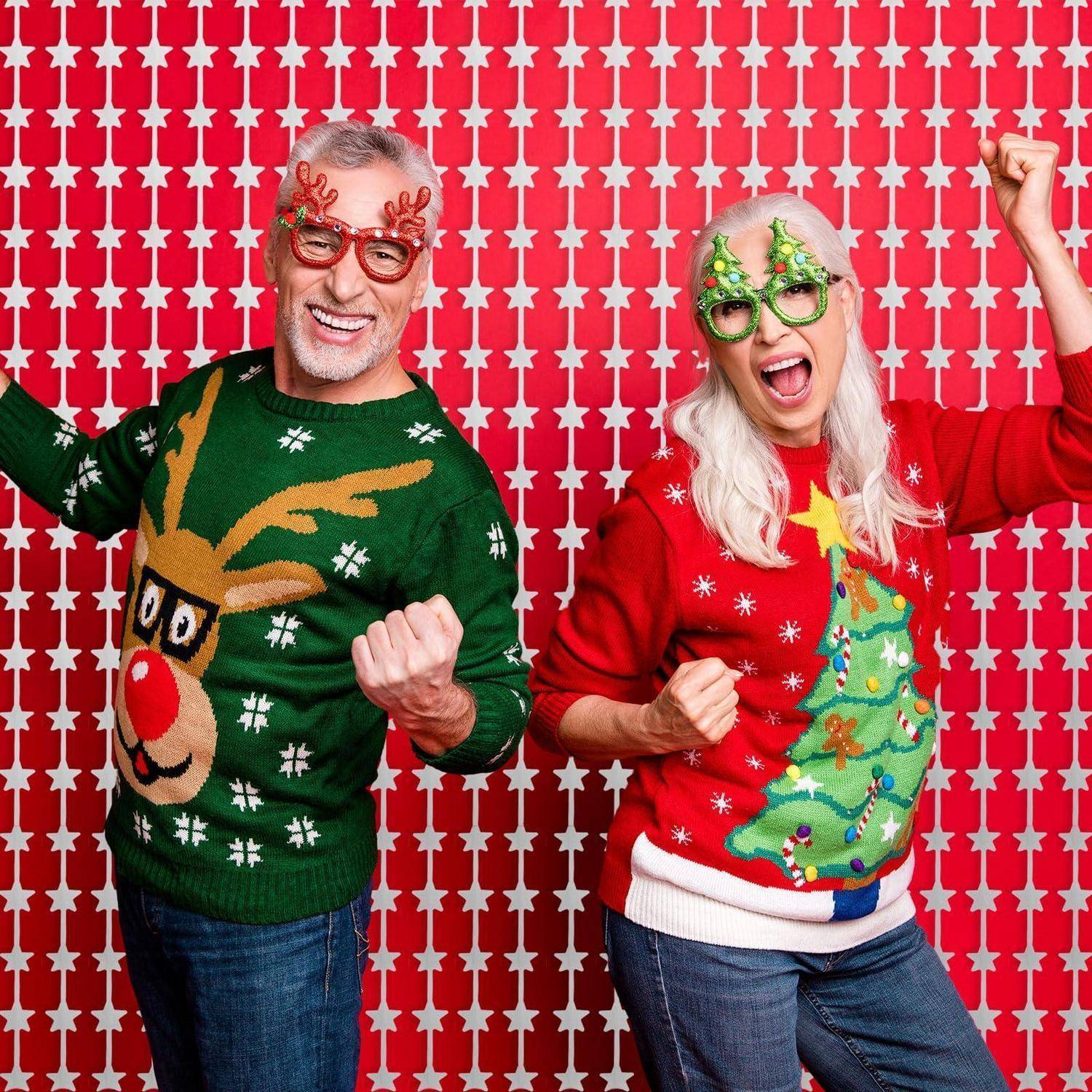 Lächelnder älterer Mann und Frau posieren in festlichen Weihnachtspullovern und Novelty-Brillen vor einem roten Hintergrund mit Sternen-Muster.