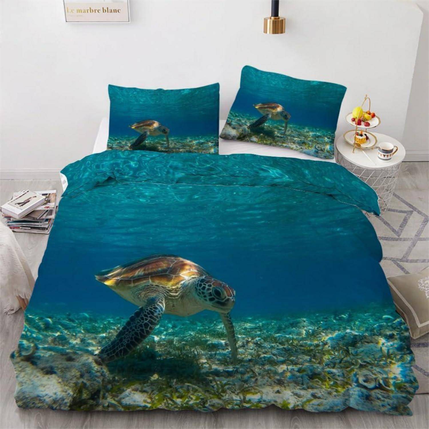 Bett mit Meeresschildkröten-Ozean-Design-Bettwäsche mit Unterwasserszene auf Bettdecke und Kissen in einem weißen Schlafzimmer.