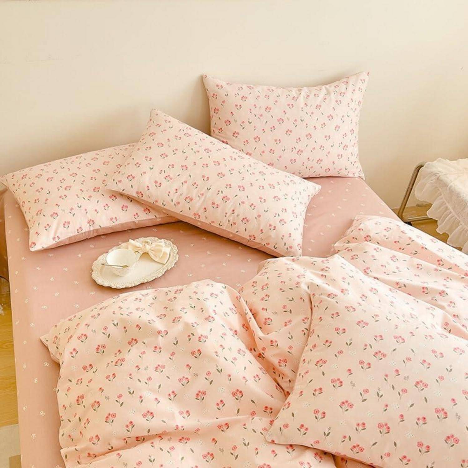 Ein ordentlich gemachtes Bett mit rosa blumigen Laken und Kissenbezügen, mit einem langen Körperkissen und einem kleinen dekorativen Tablett obenauf.