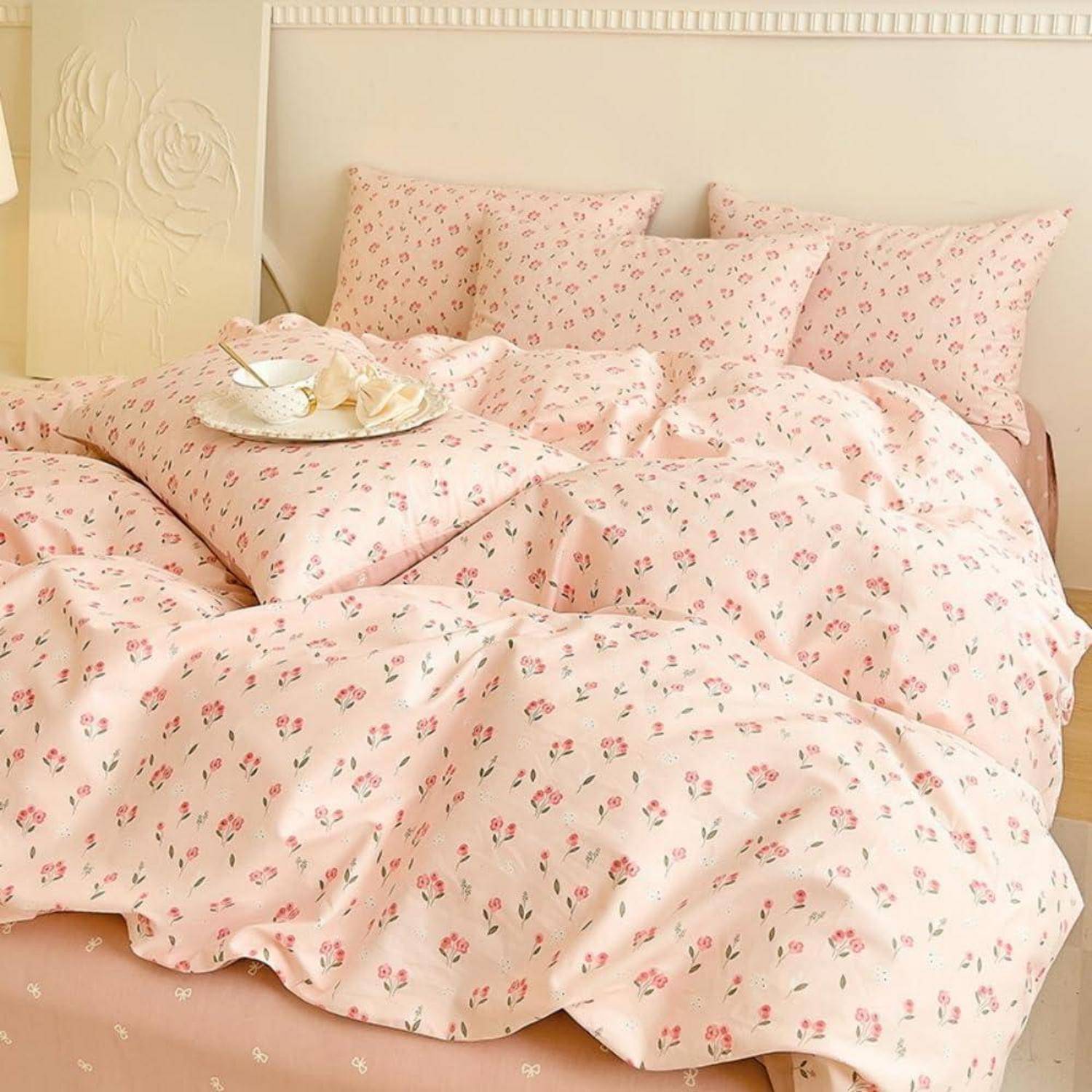 Rosa Blumenbettwäsche mit Kissen und Bettdecke auf einem ordentlich gemachtem Bett, mit einem Tablett mit Frühstück oder Tee oben drauf platziert.