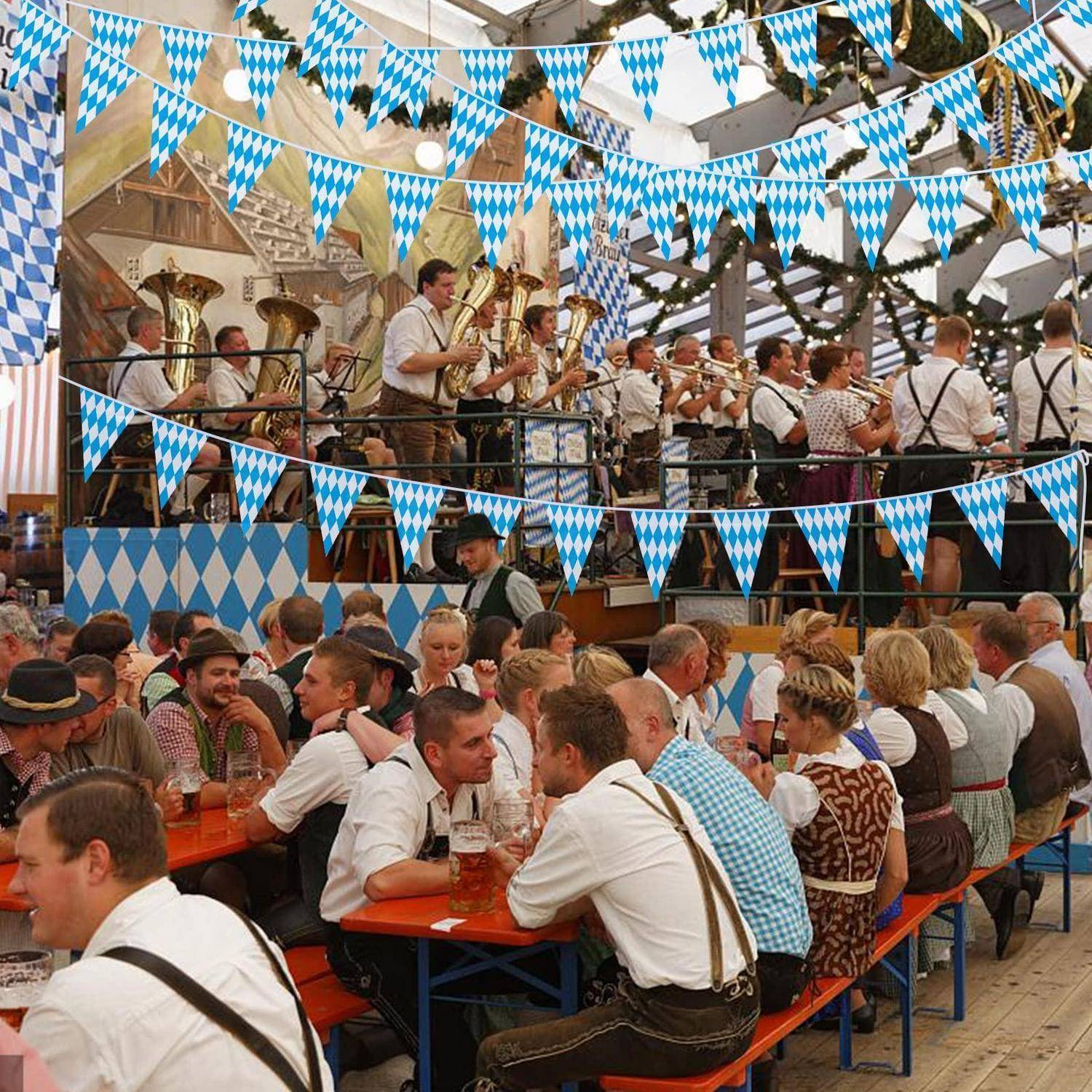 Überfülltes Oktoberfest-Bierzelt mit Blaskapelle auf einer erhöhten Plattform, blau-weiße Wimpelketten über Kopf und Menschen in traditioneller bayerischer Tracht, die an langen Tischen trinken.