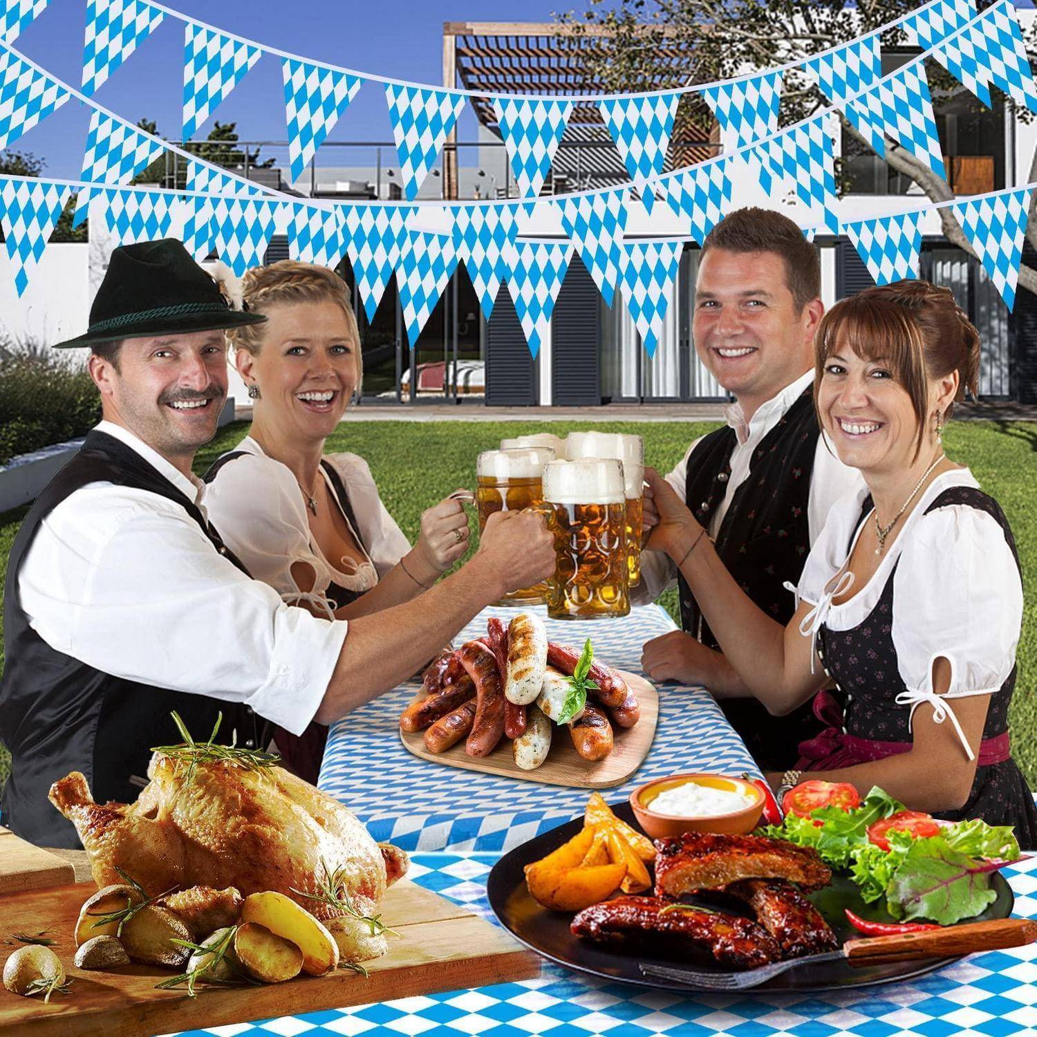 Vier Menschen in traditioneller bayerischer Tracht stoßen mit Bierkrügen an einem festlichen Außentisch an, mit Bratenspezialitäten, Würsten, Brezeln und Salat unter blau-weißer Girlande.