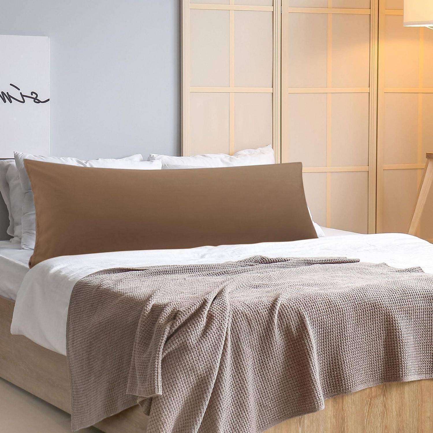 Ein ordentlich gemachtes Bett mit braunem Stützkissen und strukturierter Wurfdecke in einem weich beleuchteten modernen Schlafzimmer.