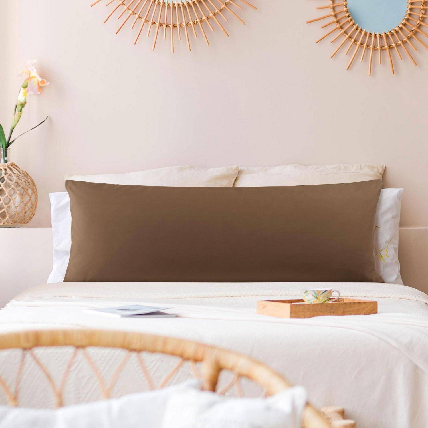 Minimales Schlafzimmer mit einem ordentlich gemachtem Bett, braunem Akzentkissen, gewebter Dekoration und warmen Sonnenschein-Spiegeln an einer blassen Wand.