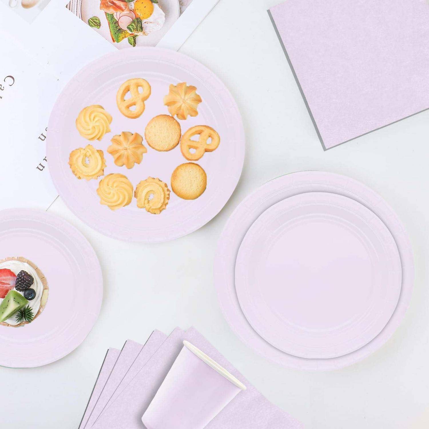 Tischgedeck für eine Pastell-Lavendel-Party mit leeren Tellern, Keksen auf einem Teller, einer Dessertschale und gefalteten Servietten auf weißem Hintergrund.