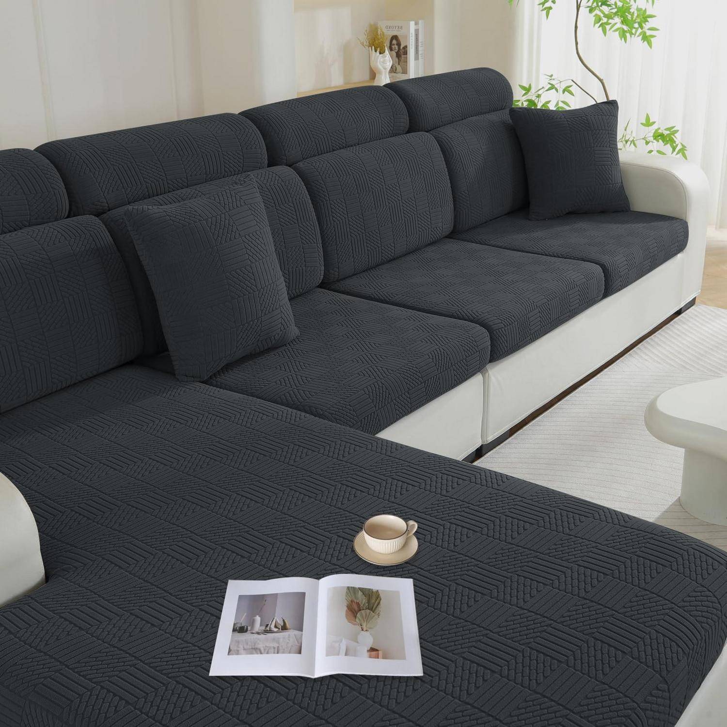 Schwarzes Ecksofa mit passender Chaiselongue und Kissen in einem hellen Wohnzimmer, mit einer offenen Zeitschrift und einer Tasse auf dem Ottomane.