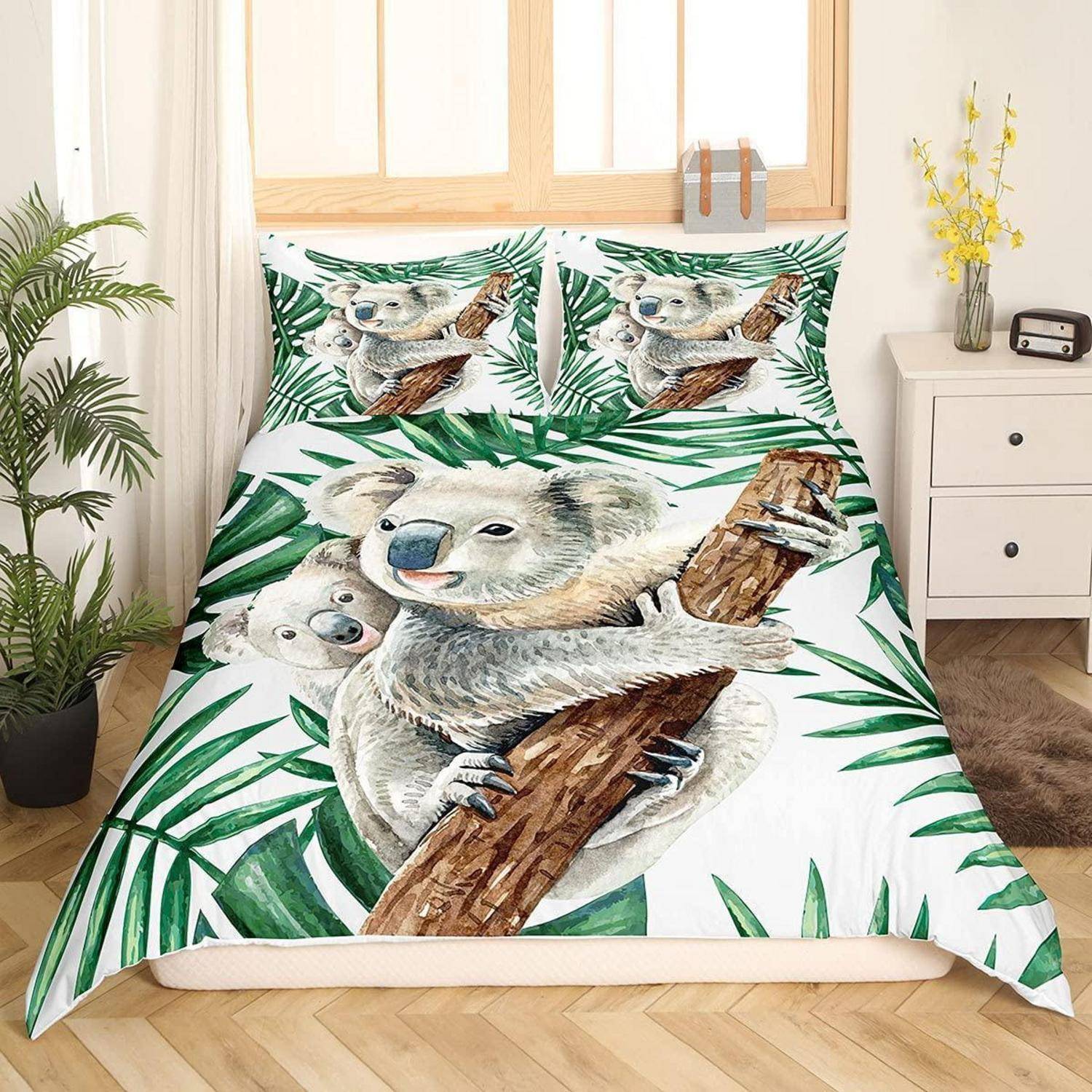 Koala-Themen-Bettwäscheset mit illustrierten Koalas und Babykoala zwischen grünen Blättern auf einem Bett in einem hellen Schlafzimmer.