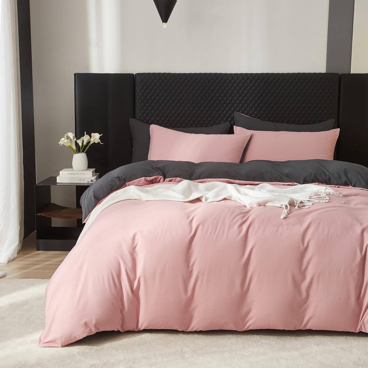 Ein ordentlich gemachtes Bett mit rosa Bettwäsche und dunklen Kissen in einem modernen Schlafzimmer, mit einem schwarzen Kopfteil und einem kleinen Nachttisch, auf dem Blumen und Bücher stehen.