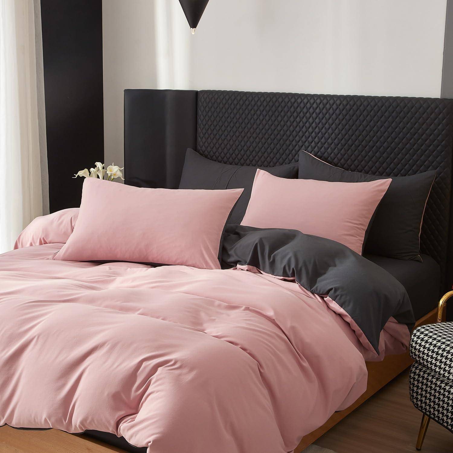 Rosa Bettwäsche mit schwarzen und grauen Kissen auf einem modernen Bett mit dunklem gepolstertem Kopfteil.