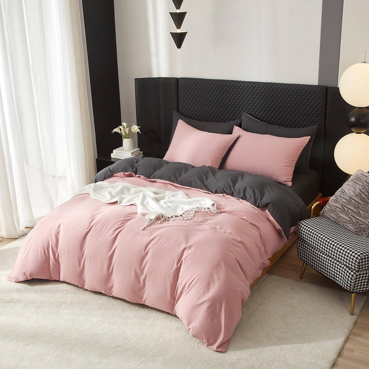 Modernes Schlafzimmer mit ordentlich gemachtem Bett in rosa und anthrazitfarbener Bettwäsche, schwarzem gestepptem Kopfteil, Nachttischlampe und gemustertem Stuhl.